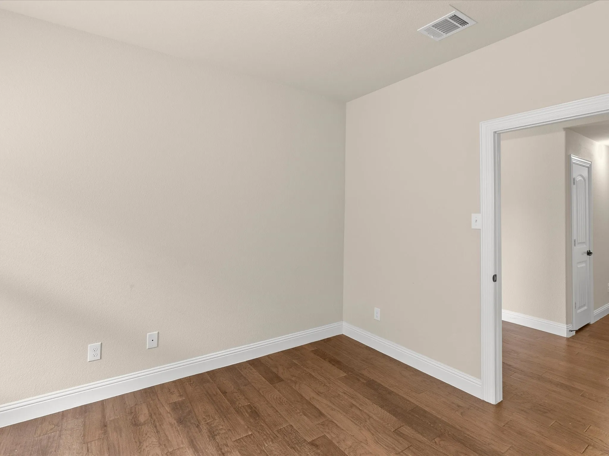 Wood-finish flooring, neutral wall color, white trim, and a doorway with casing