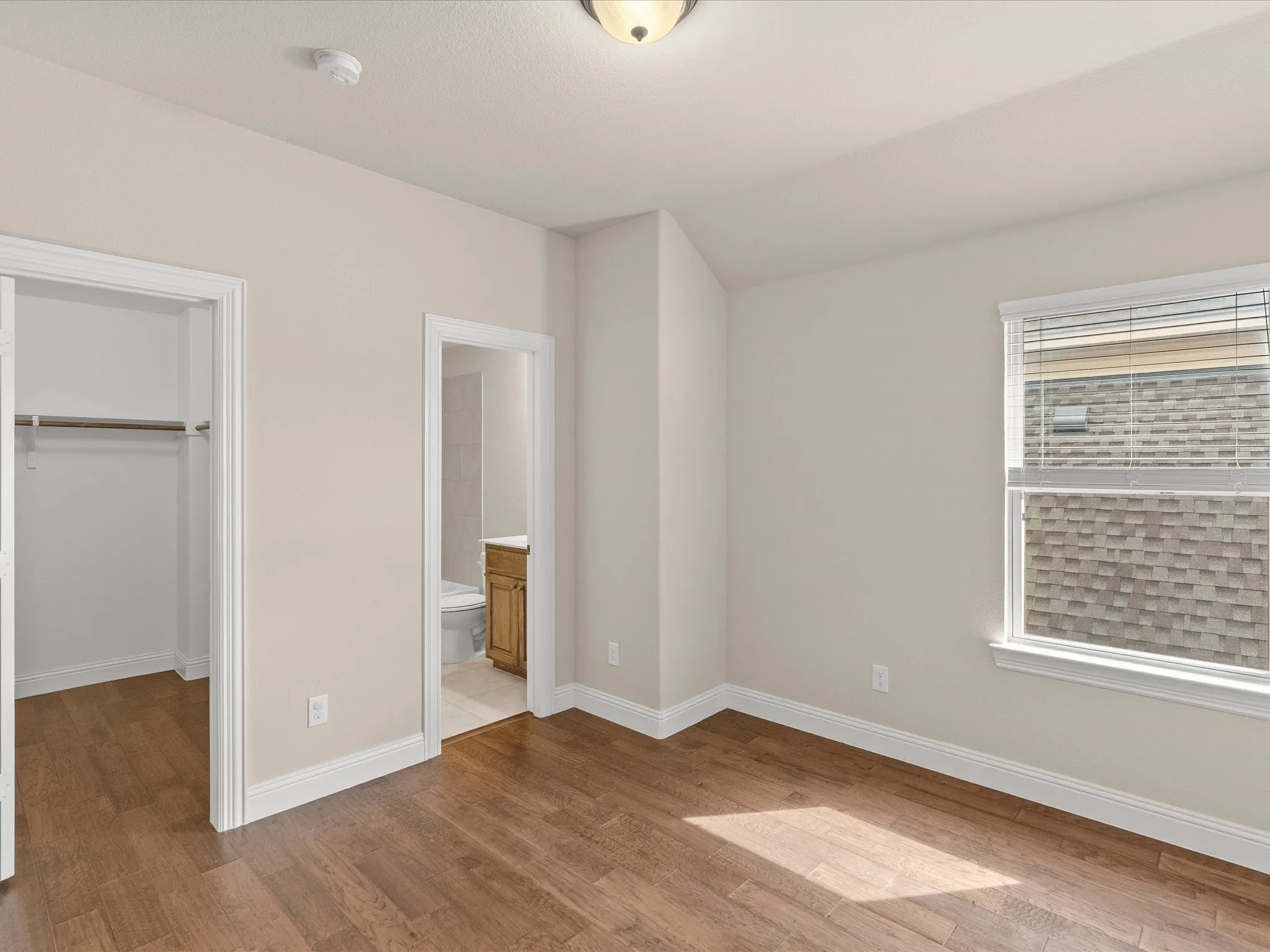 Wood-finish flooring, white trim, and a window with blinds