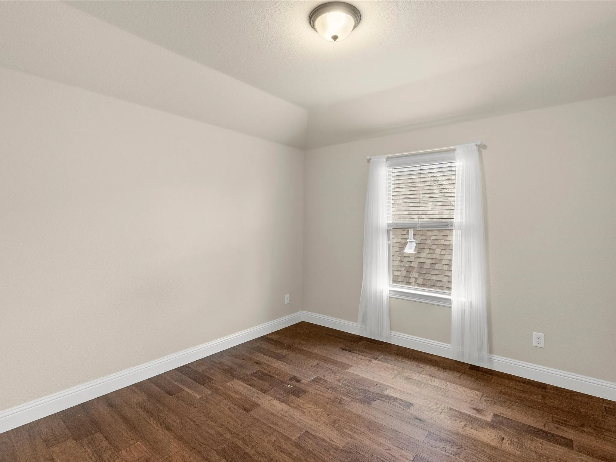 Vaulted ceiling, wood-finish flooring, single window with blinds, and a flush-mount ceiling light