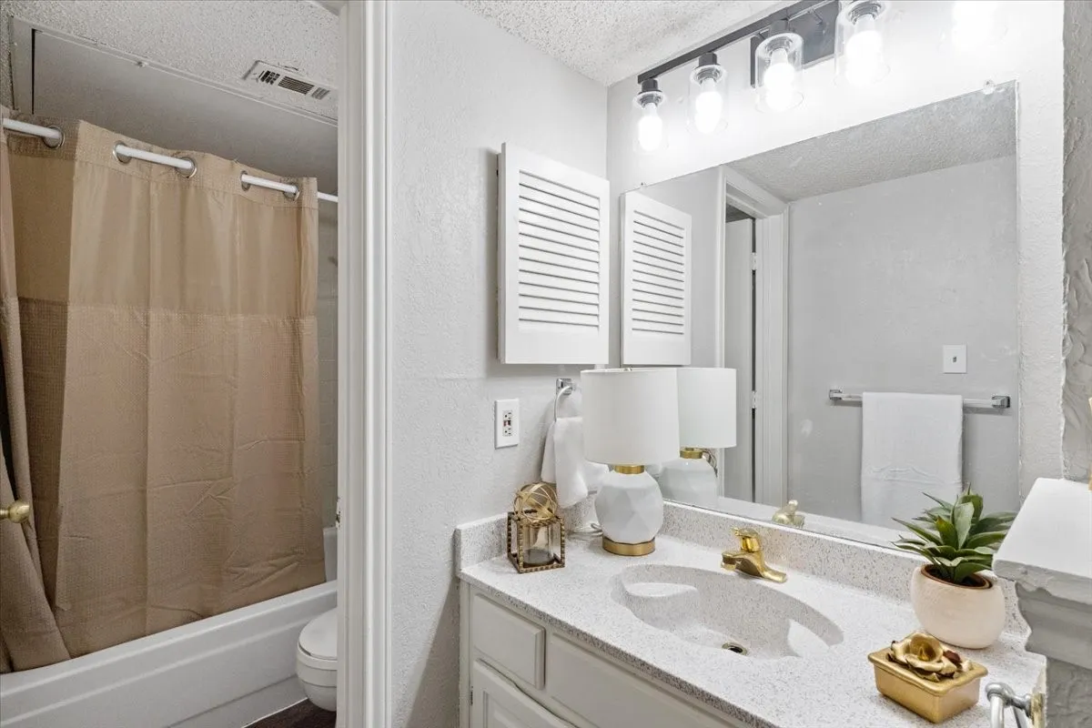 White vanity with a speckled countertop and integrated sink, gold-finish faucet, and overhead track lighting