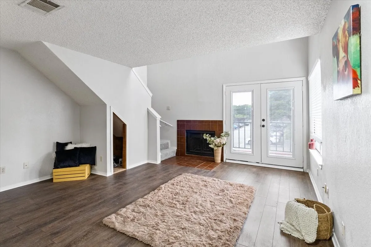 Vaulted ceiling, wood-finish flooring, staircase, built-in storage under stairs, and a fireplace with a tile surround