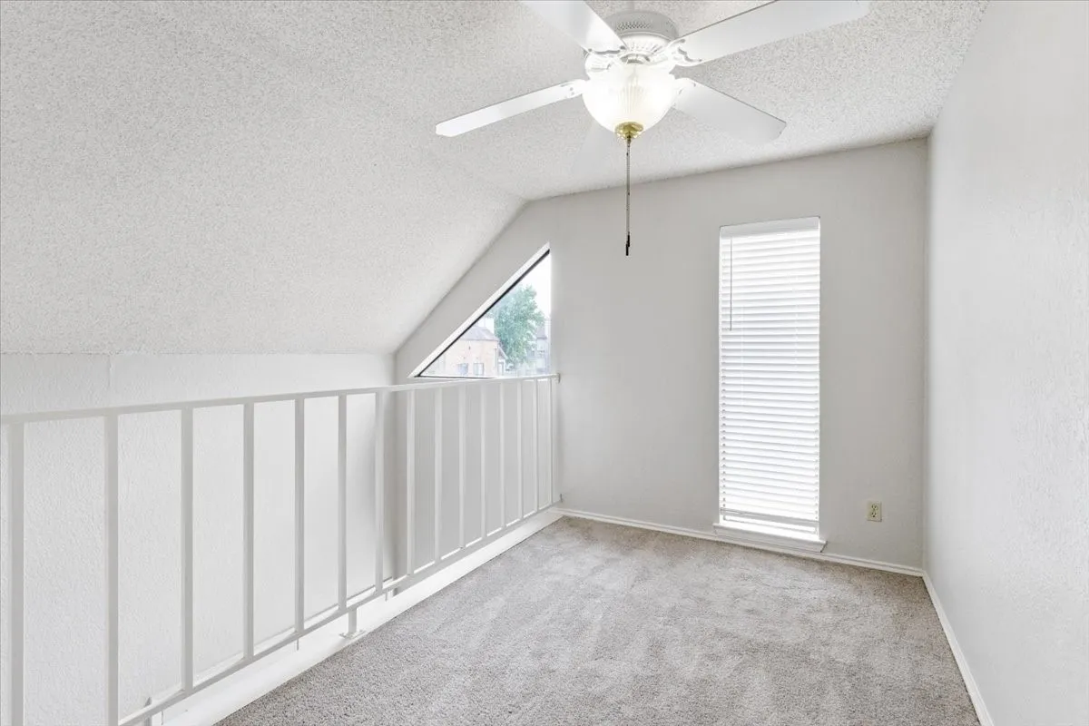 Carpeted loft space with an angled ceiling, ceiling fan, and two windows with blinds