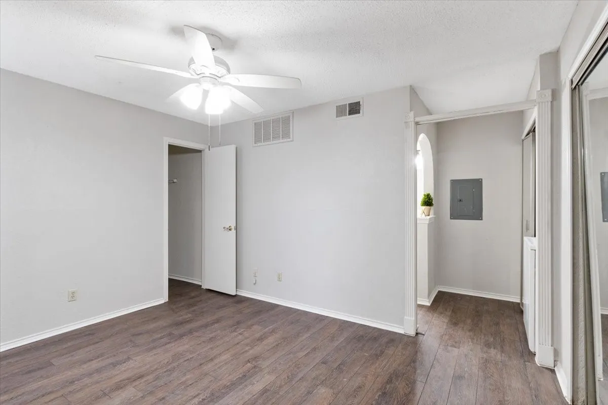 Wood-finish flooring, white ceiling fan, interior door, mirrored closet doors, and an arched alcove