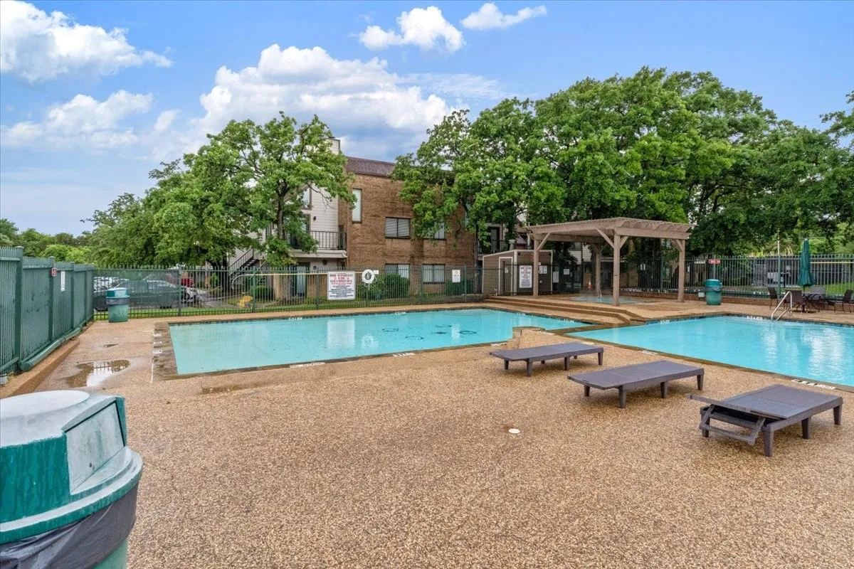 Expansive pool deck with multiple swimming pools, a shaded pergola, and surrounding mature trees
