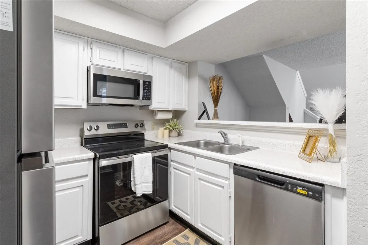 Stainless steel appliances, white cabinetry, double basin sink, and wood-finish flooring