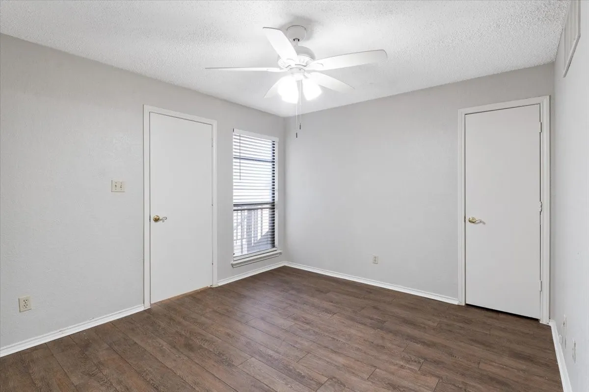 Wood-finish flooring, white ceiling fan with integrated lighting, window with blinds, and two panel doors with brass hardware