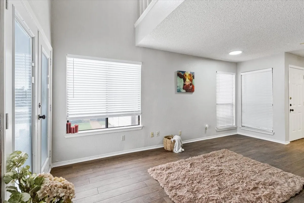 Vaulted ceiling, wood-finish flooring, white walls, multiple windows with blinds, and a built-in circular ceiling light