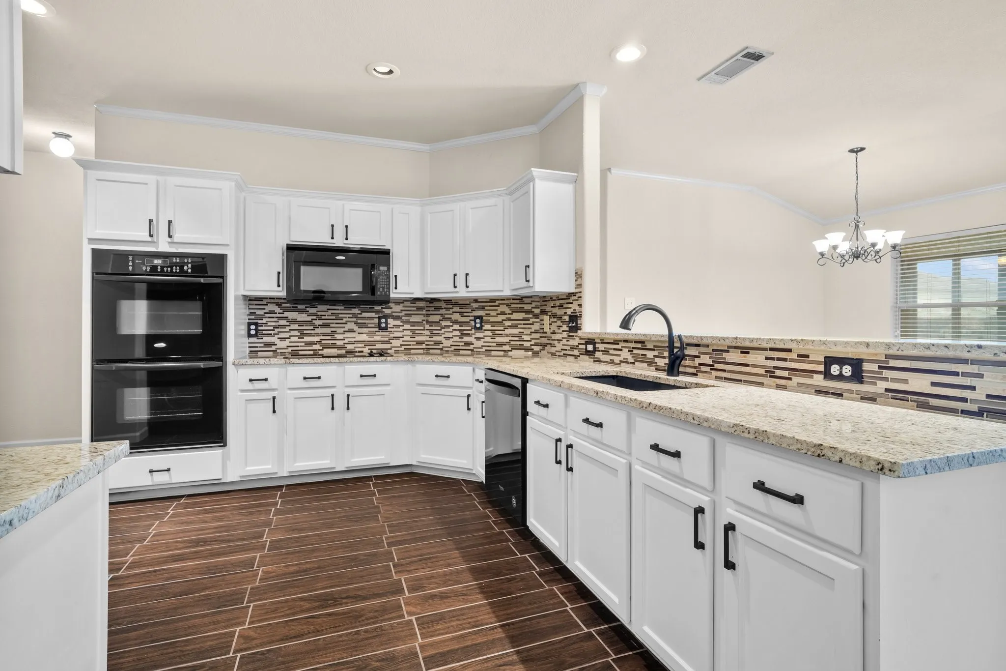 Kitchen featuring white shaker-style cabinetry, light-toned countertops, a mosaic tile backsplash, black double wall ovens, and wood-finish flooring