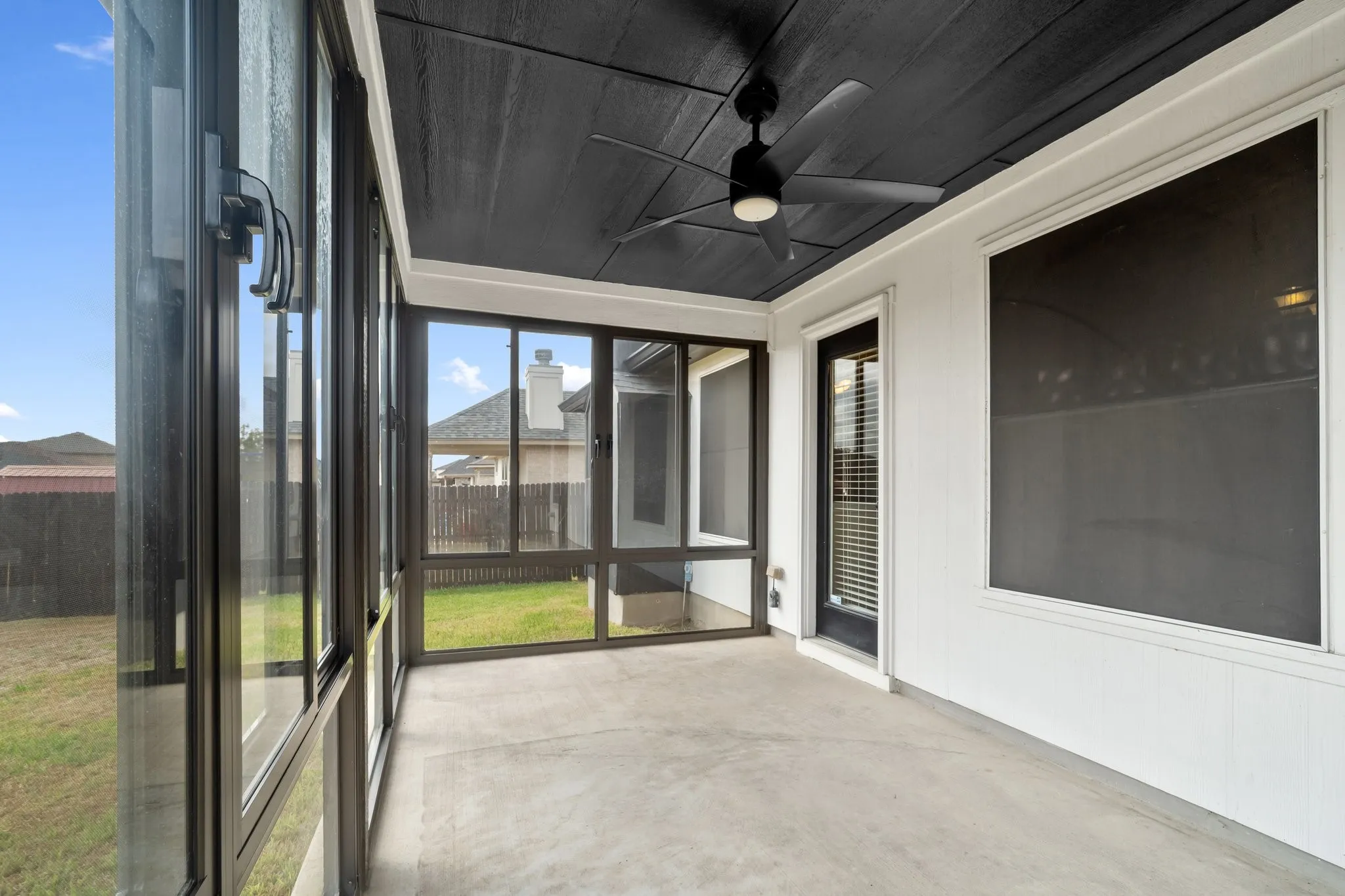 Screened-in porch featuring a concrete floor, black ceiling fan, and white exterior wall with dark trim