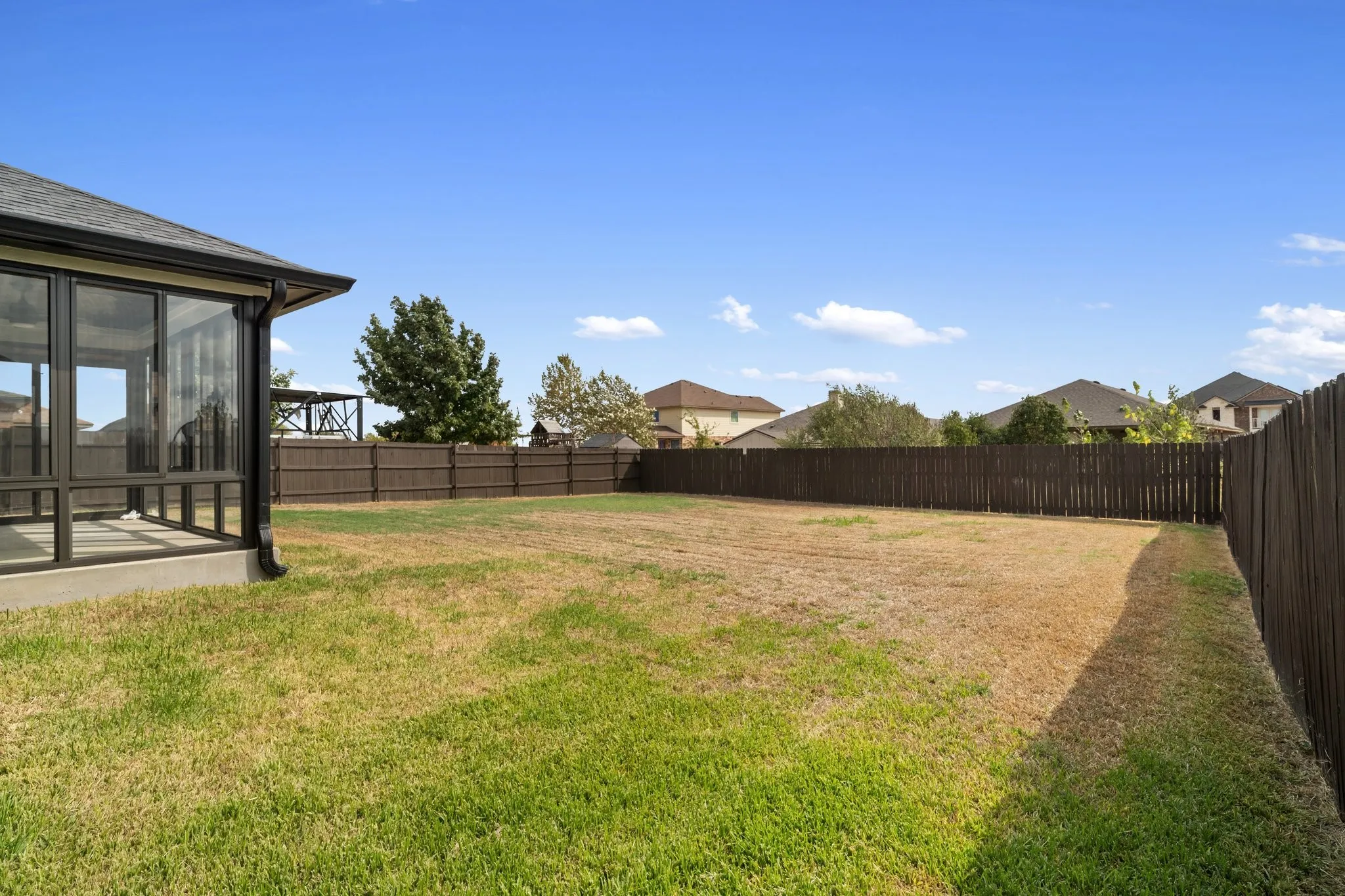 Expansive fenced backyard featuring a sunroom addition with large glass panels, a dark wood privacy fence, and a large lawn area