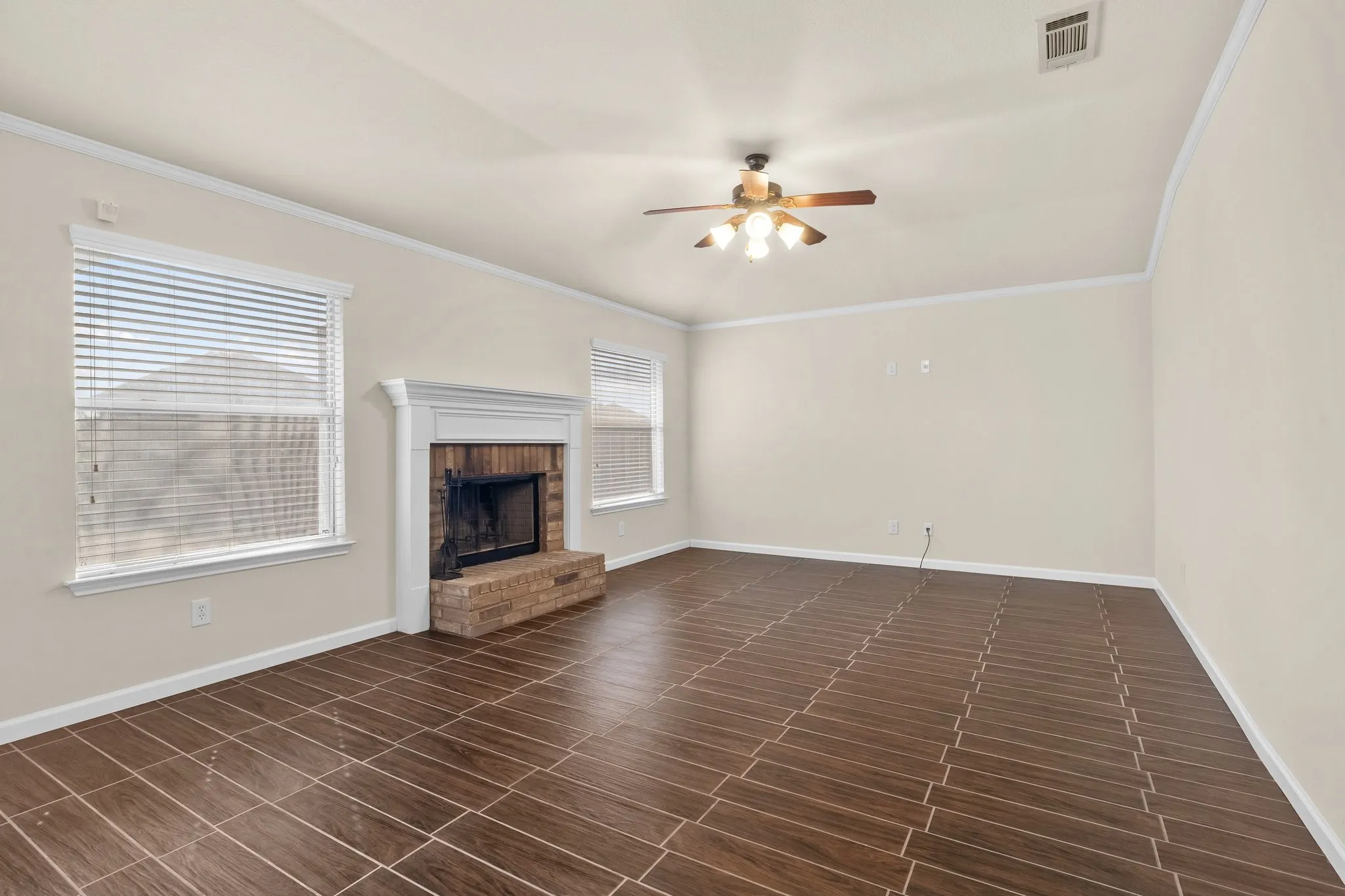 Wood-finish tile flooring complemented by a brick fireplace with a classic mantel, ceiling fan, and white trim