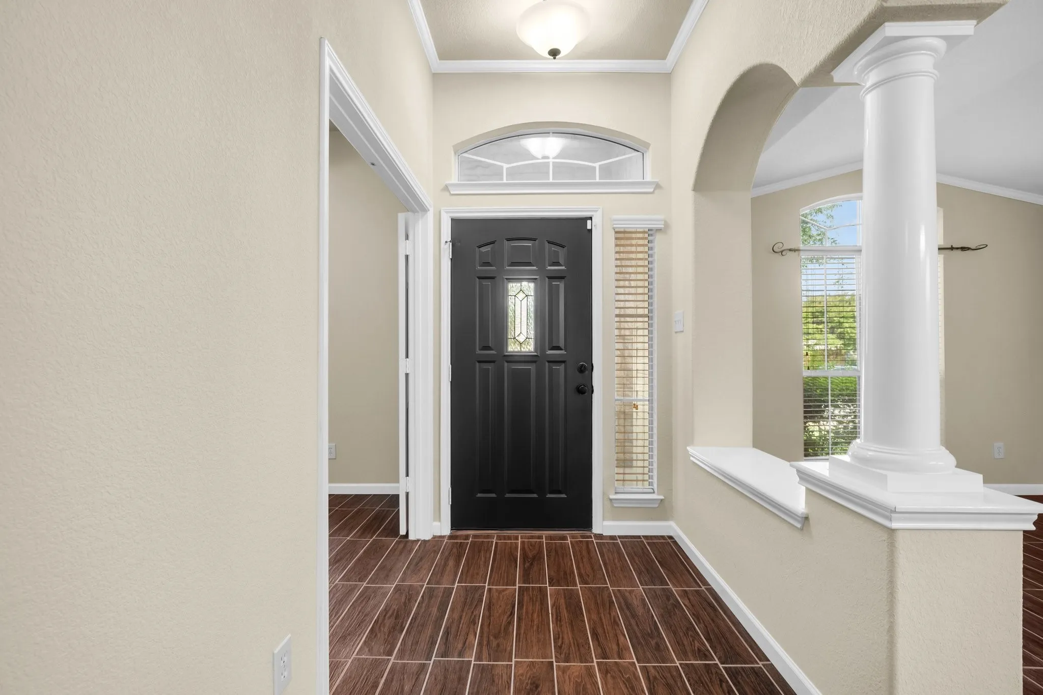 Entryway featuring wood-finish tile flooring, a dark paneled door with decorative glass, and an arched doorway
