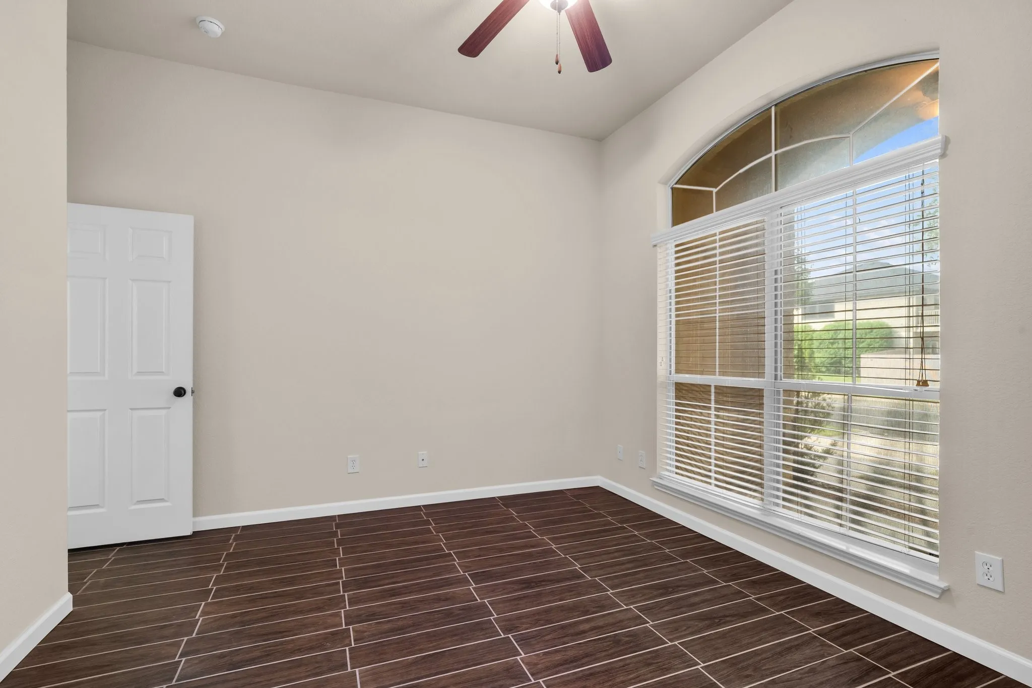 Arch-top window with blinds, wood-finish flooring, ceiling fan with integrated lighting, and a white paneled door
