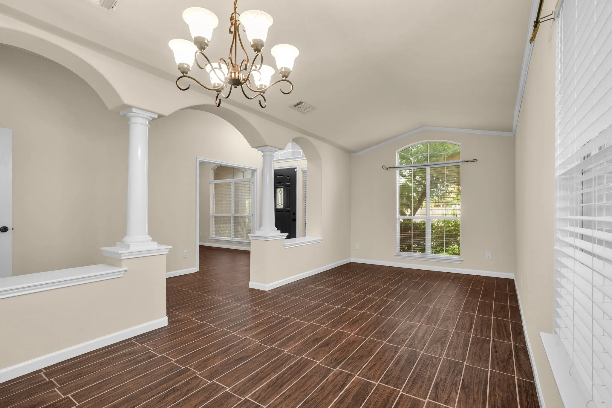 Elegant open-concept living space featuring soaring ceilings with decorative crown molding, a brass multi-arm chandelier, and abundant natural light from arched windows