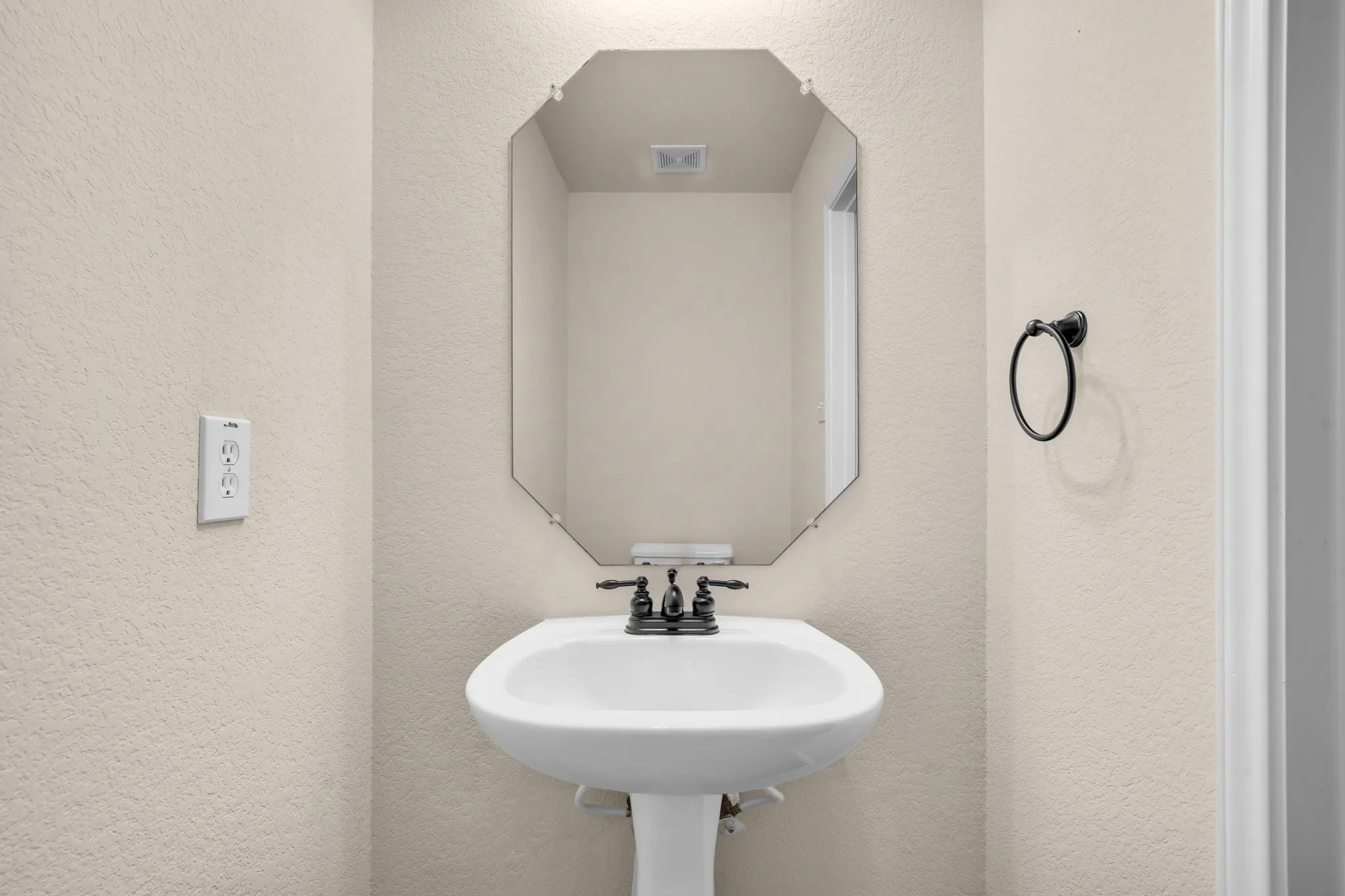 Pedestal sink with a matte black faucet, complemented by an octagonal mirror and a round towel ring
