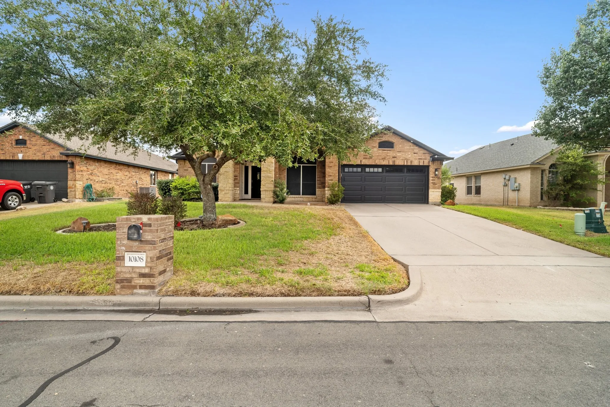 Brick exterior home with an attached garage, concrete driveway, and a mature front yard tree
