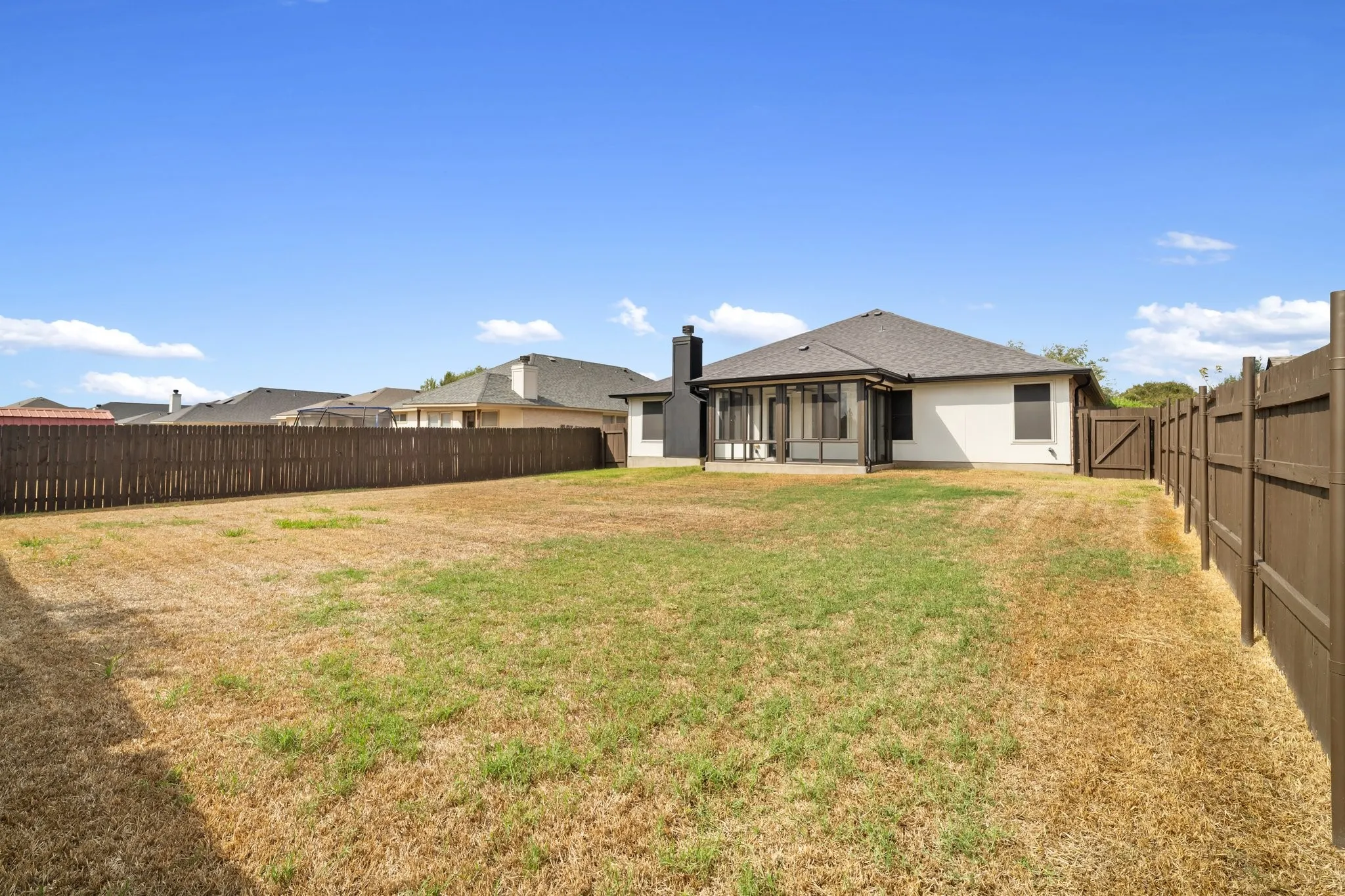 Expansive backyard featuring a screened-in patio, wood fencing, and a side gate