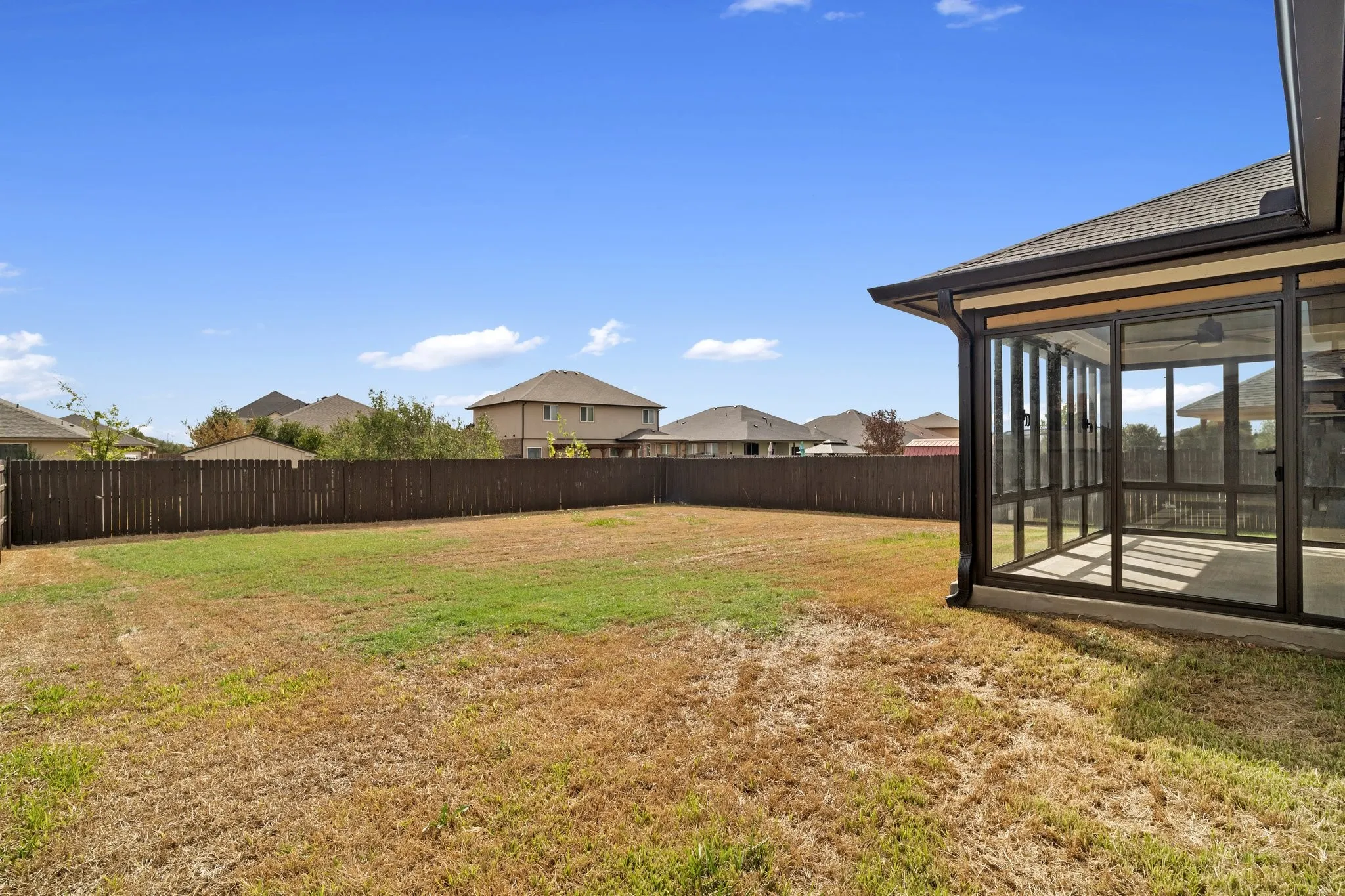 Expansive backyard with a full privacy fence and a screened-in patio featuring a ceiling fan