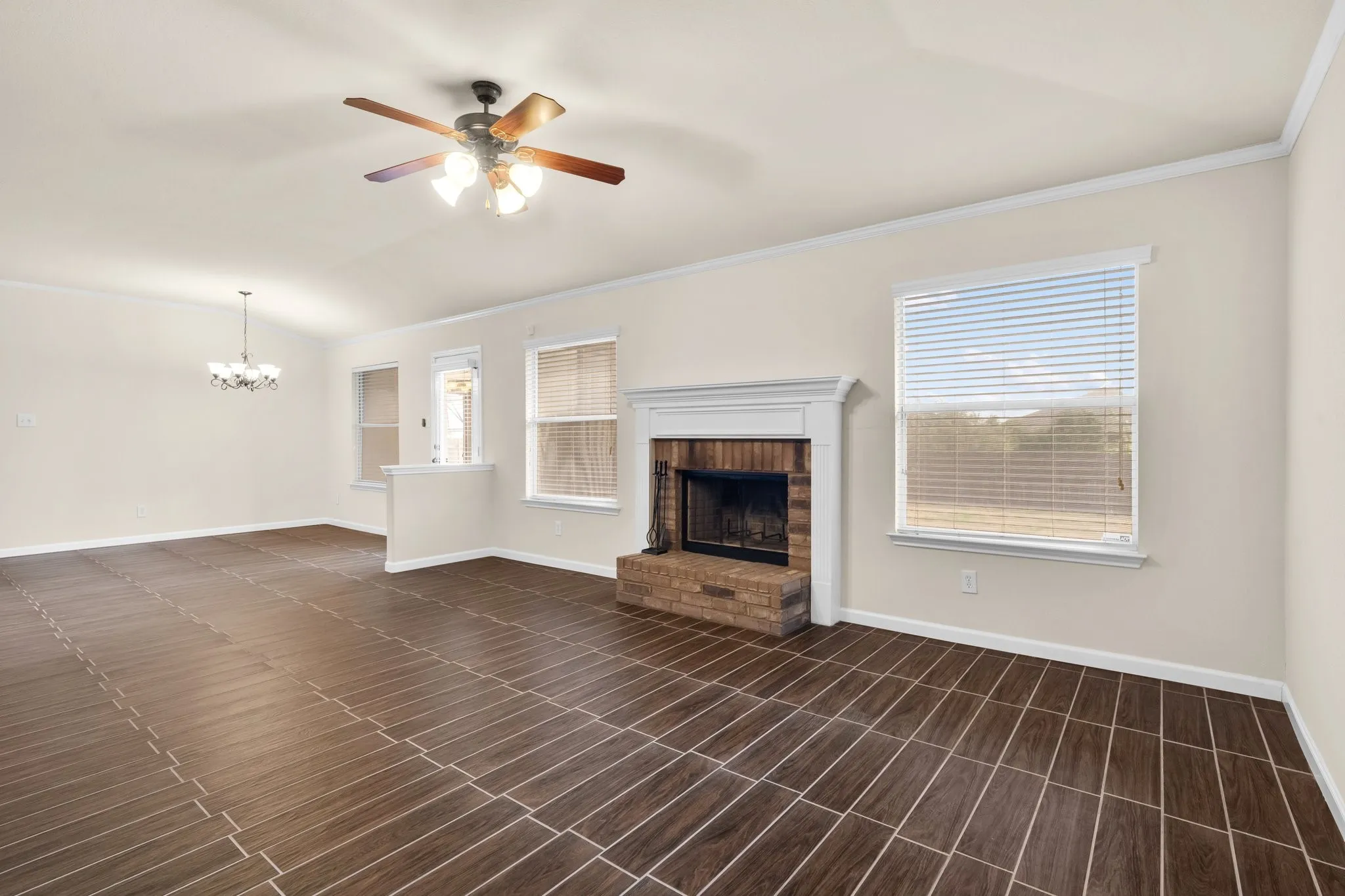 Expansive living area featuring large format tile flooring, a brick fireplace with a white mantel, and multiple windows