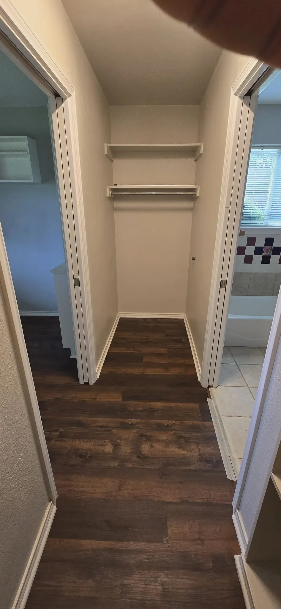 Hallway featuring wood-finish flooring, two white interior doors, and a built-in closet with shelving and a hanging rod