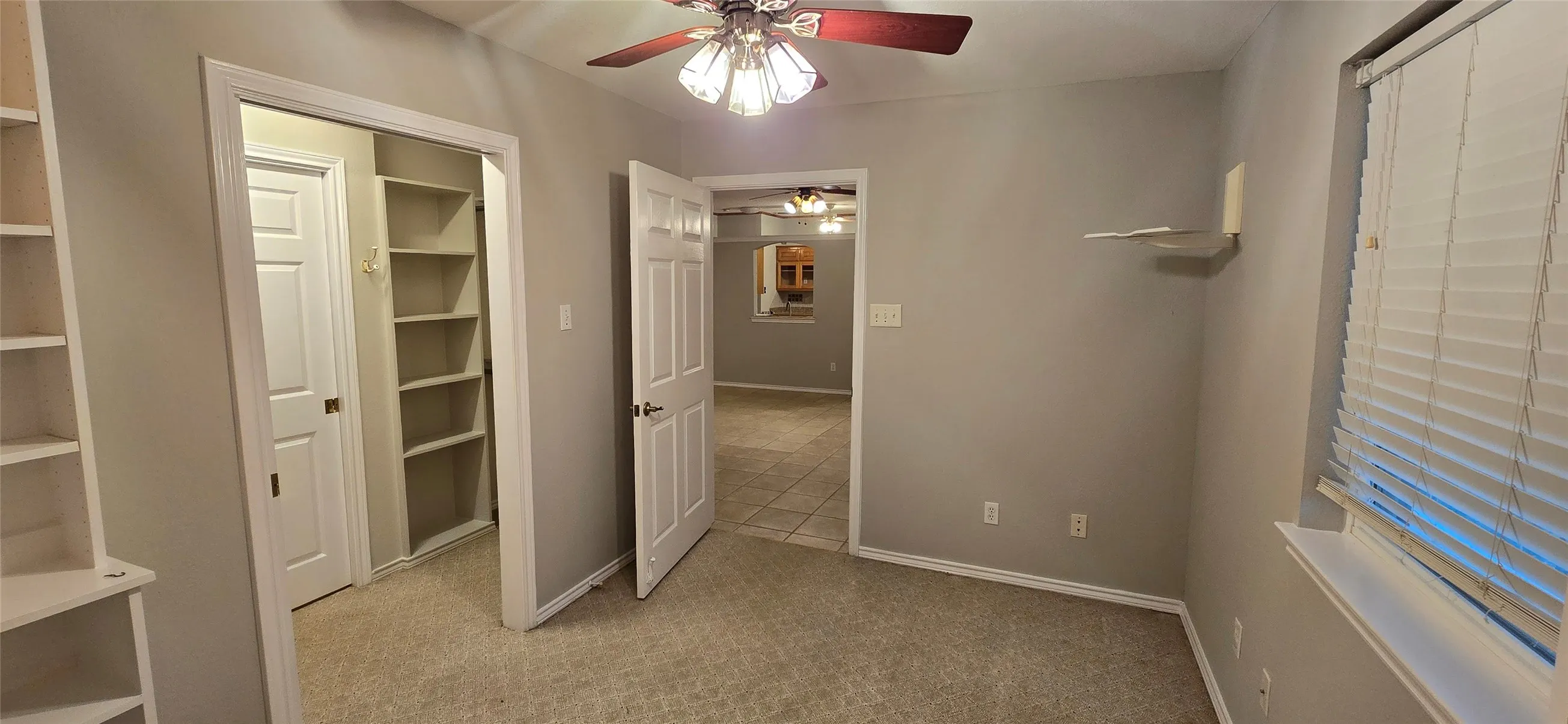 Built-in shelving, ceiling fan with light fixture, window with blinds, and carpeted flooring