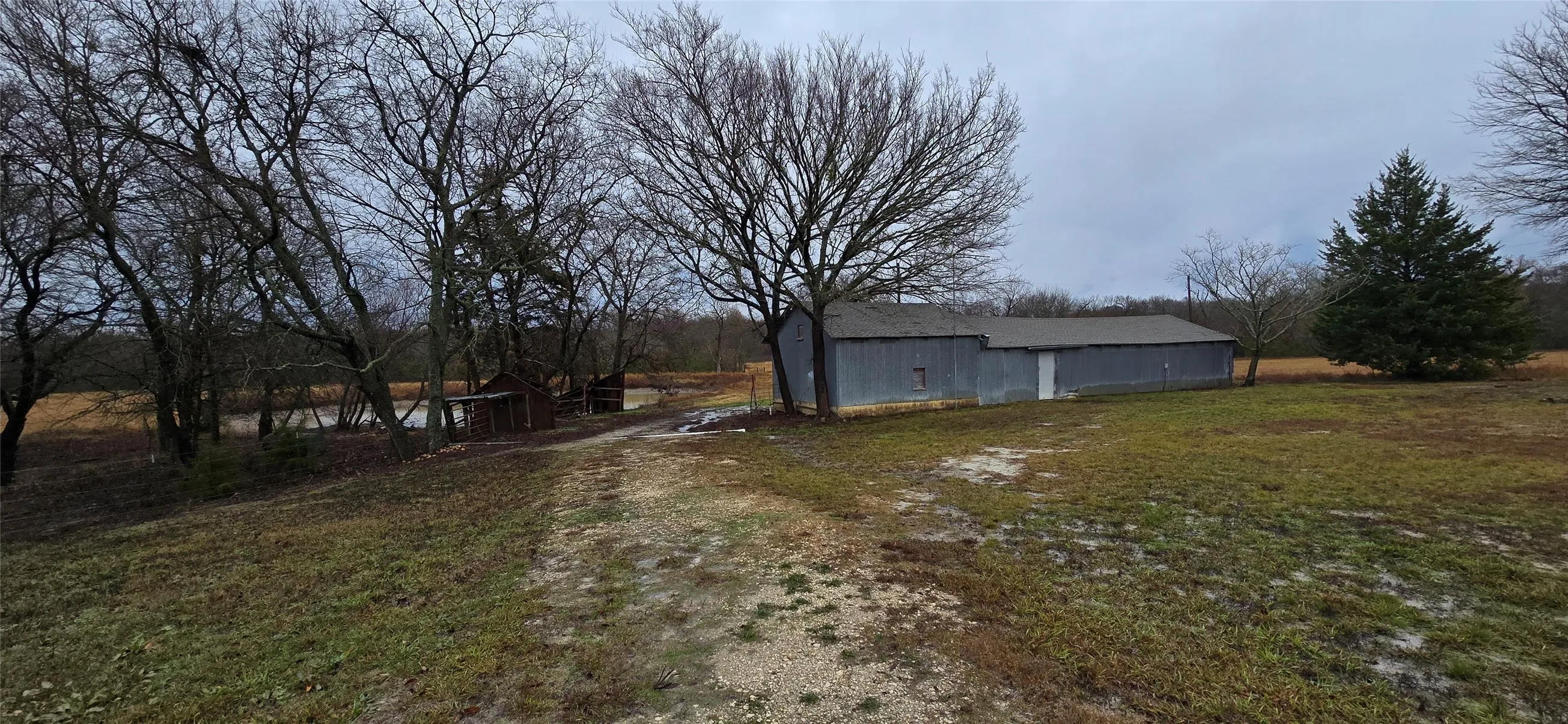 Large outbuilding with a gray metal roof and siding, surrounded by mature trees
