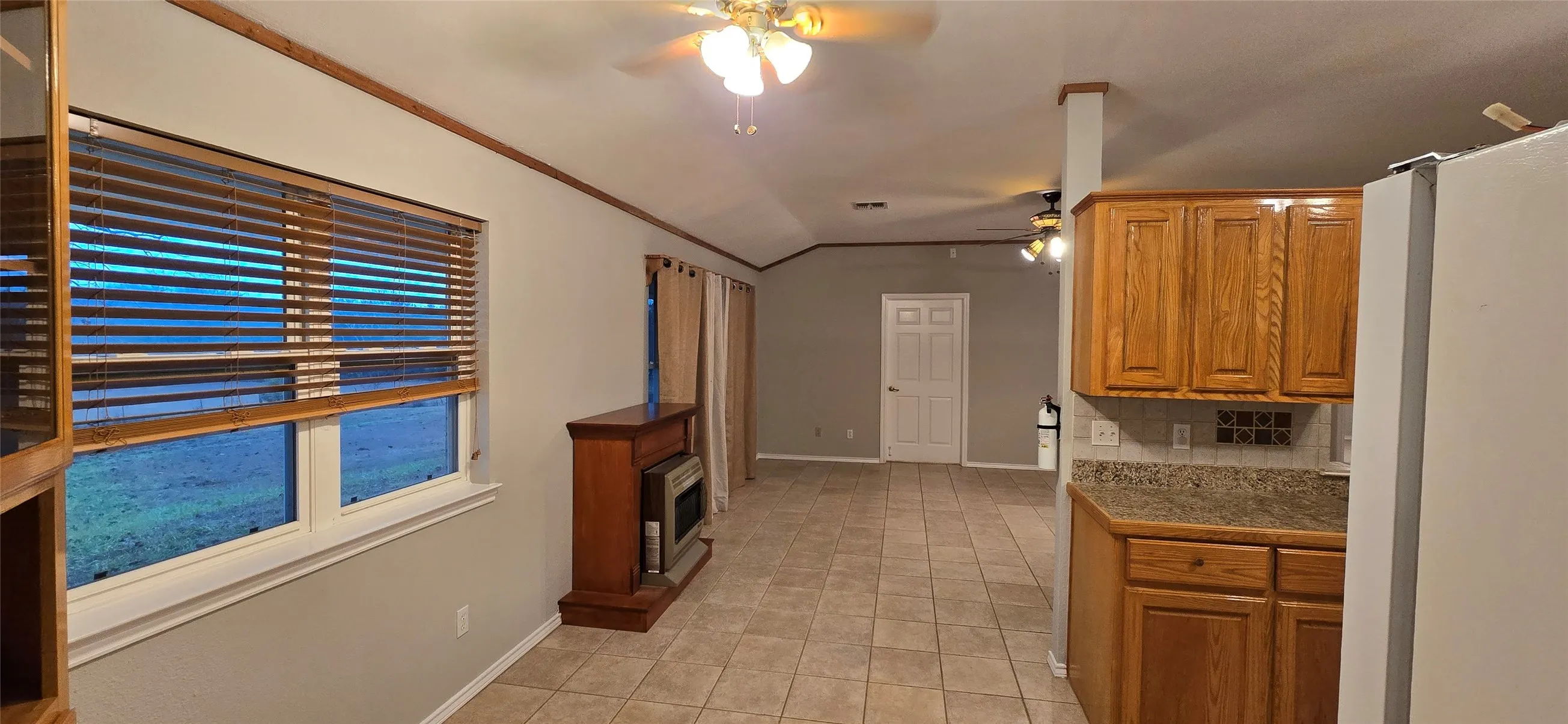Open concept living space featuring tile flooring, vaulted ceilings, and natural wood-finish cabinetry with stone-finish countertops