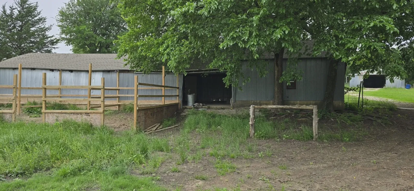 Barn structure with corrugated metal siding, an open entryway, and an attached wood-fenced enclosure