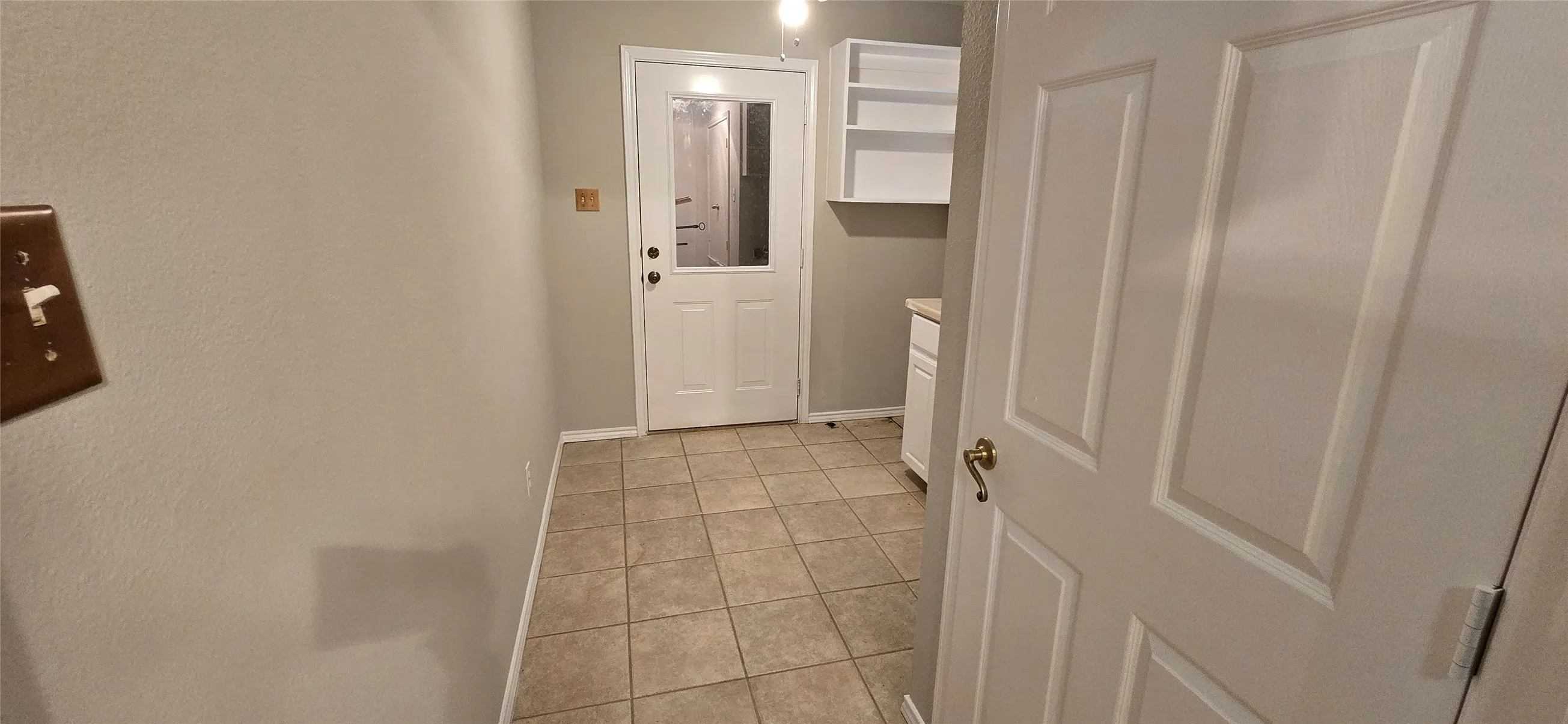 Tile flooring, white door with glass panel, white built-in shelving, and a white cabinet with a light-toned countertop