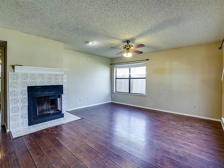 Spacious room with wood-finish flooring, a decorative fireplace with patterned tile surround, and a ceiling fan
