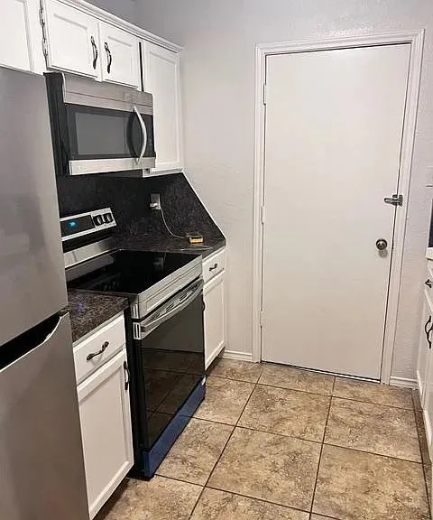 White cabinetry with dark contrasting hardware, dark countertops, built-in microwave, stainless steel refrigerator, and tiled flooring