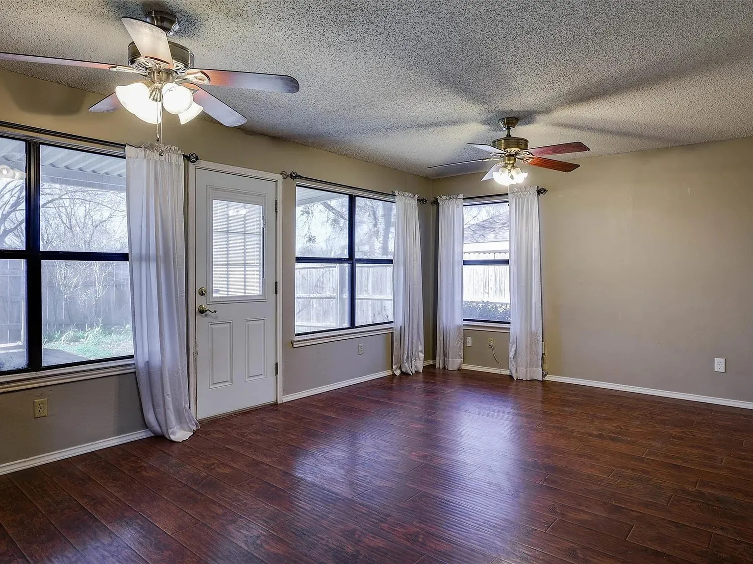 Wood-finish flooring, multiple windows, ceiling fans with integrated lighting, and a rear exterior door