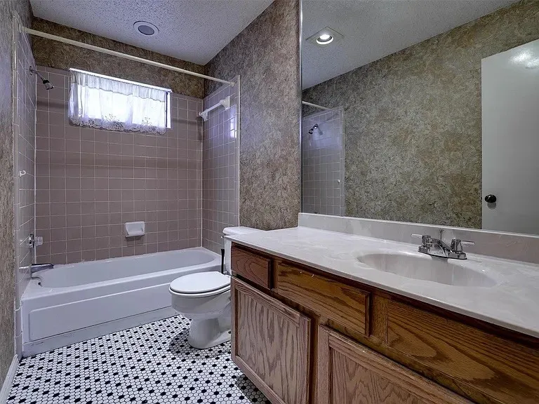 Bathroom featuring a single vanity with an integrated sink, a large wall-mounted mirror, a bathtub with a shower, and hexagonal mosaic floor tiling