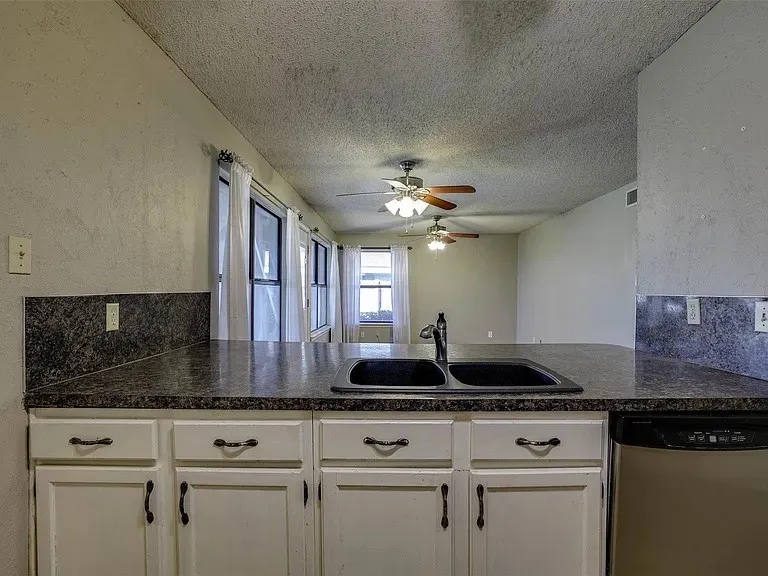 Kitchen island with a double basin sink, dark stone-look countertops, and white cabinetry with dark hardware