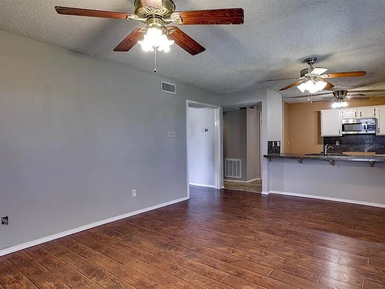 Wood-finish flooring throughout, multiple ceiling fans with integrated lighting, white kitchen cabinetry, stainless steel microwave, and dark-toned countertops
