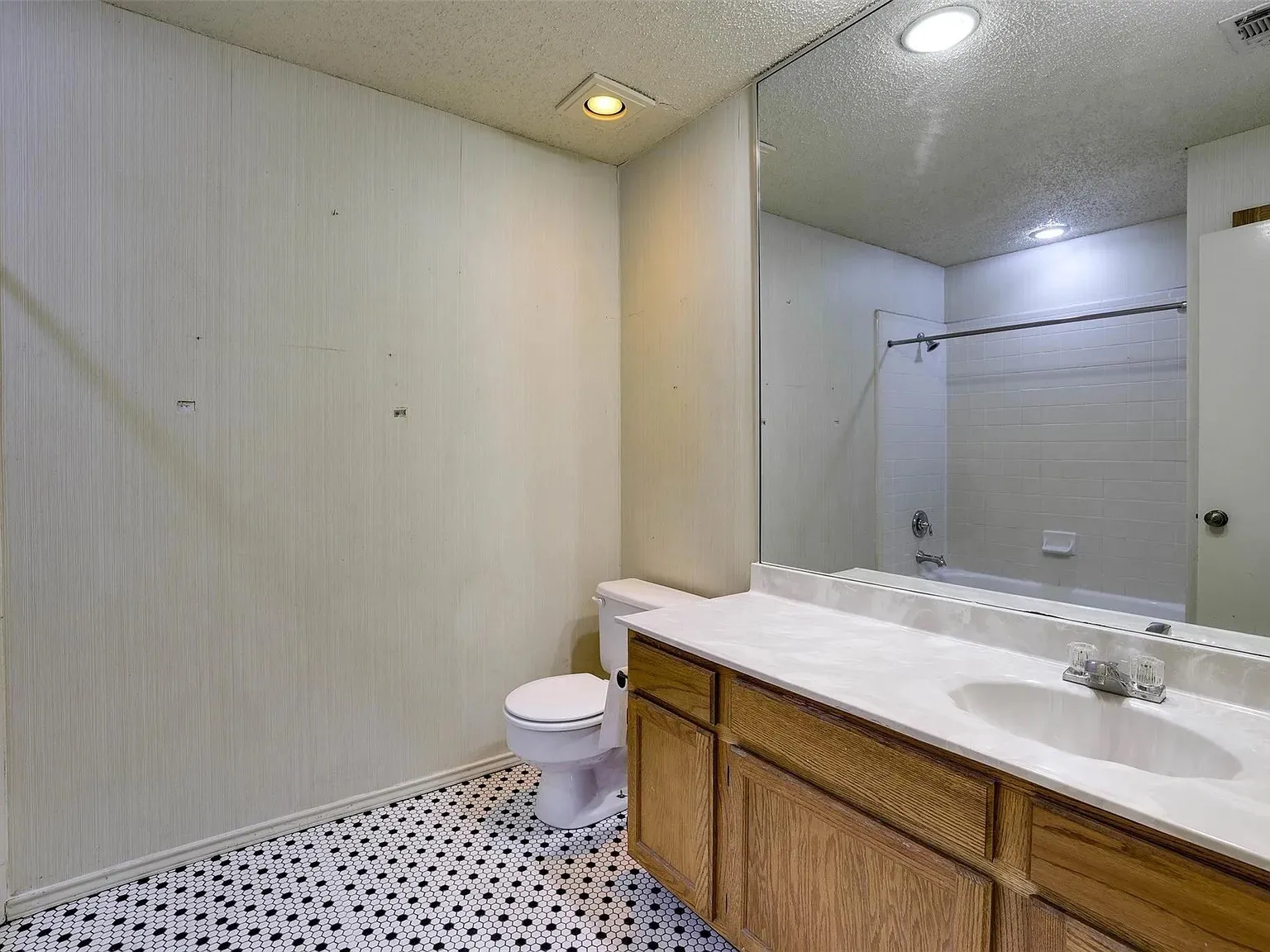 Bathroom featuring a wood-finish vanity with an integrated sink, a full-width mirror, and a white tile bathtub surround