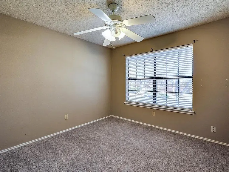 Neutral wall paint, textured ceiling, carpeted flooring, window with blinds, and a ceiling fan with integrated lighting