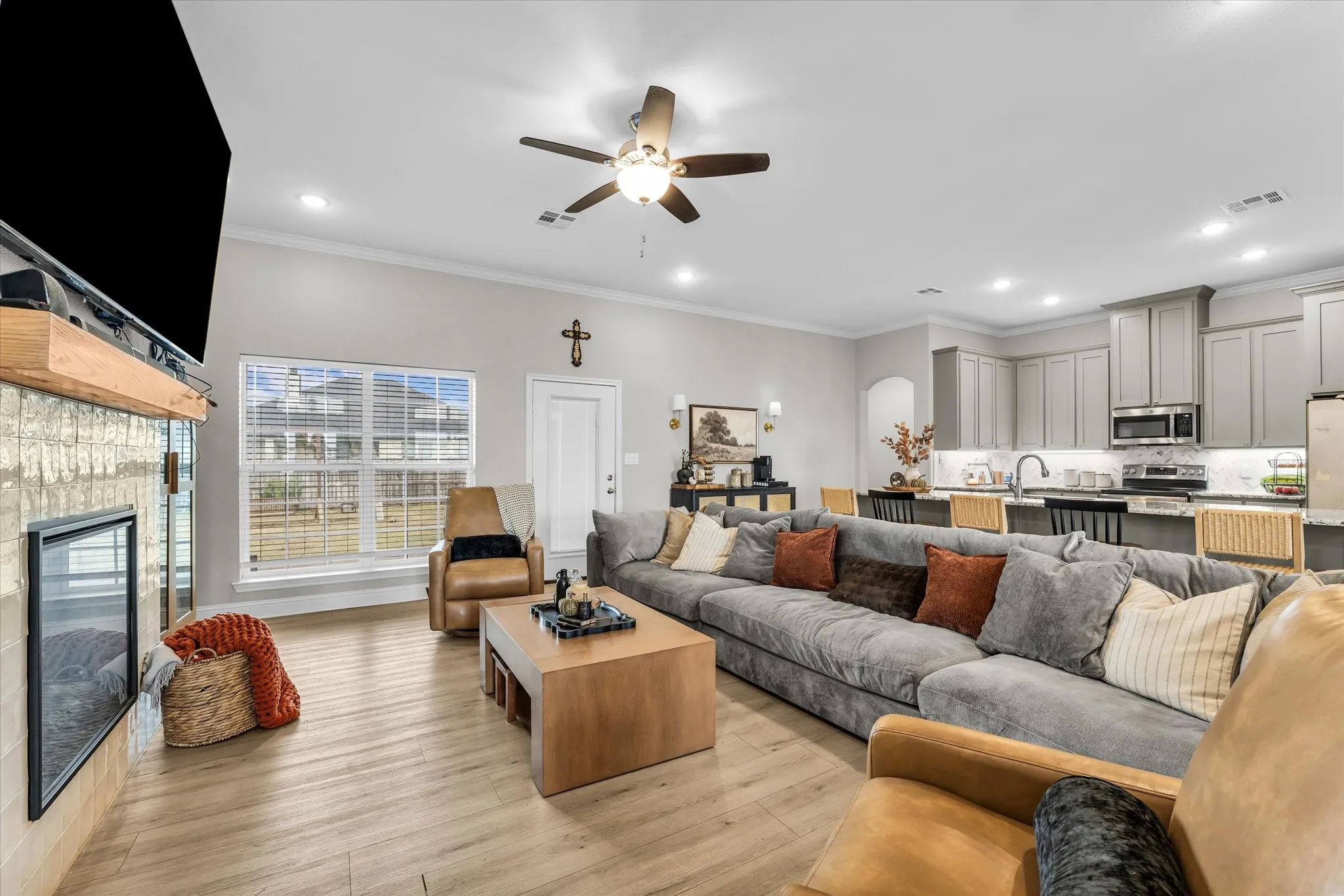 Open-concept living area with wood-finish flooring, a contemporary fireplace with a light brick surround, and a ceiling fan