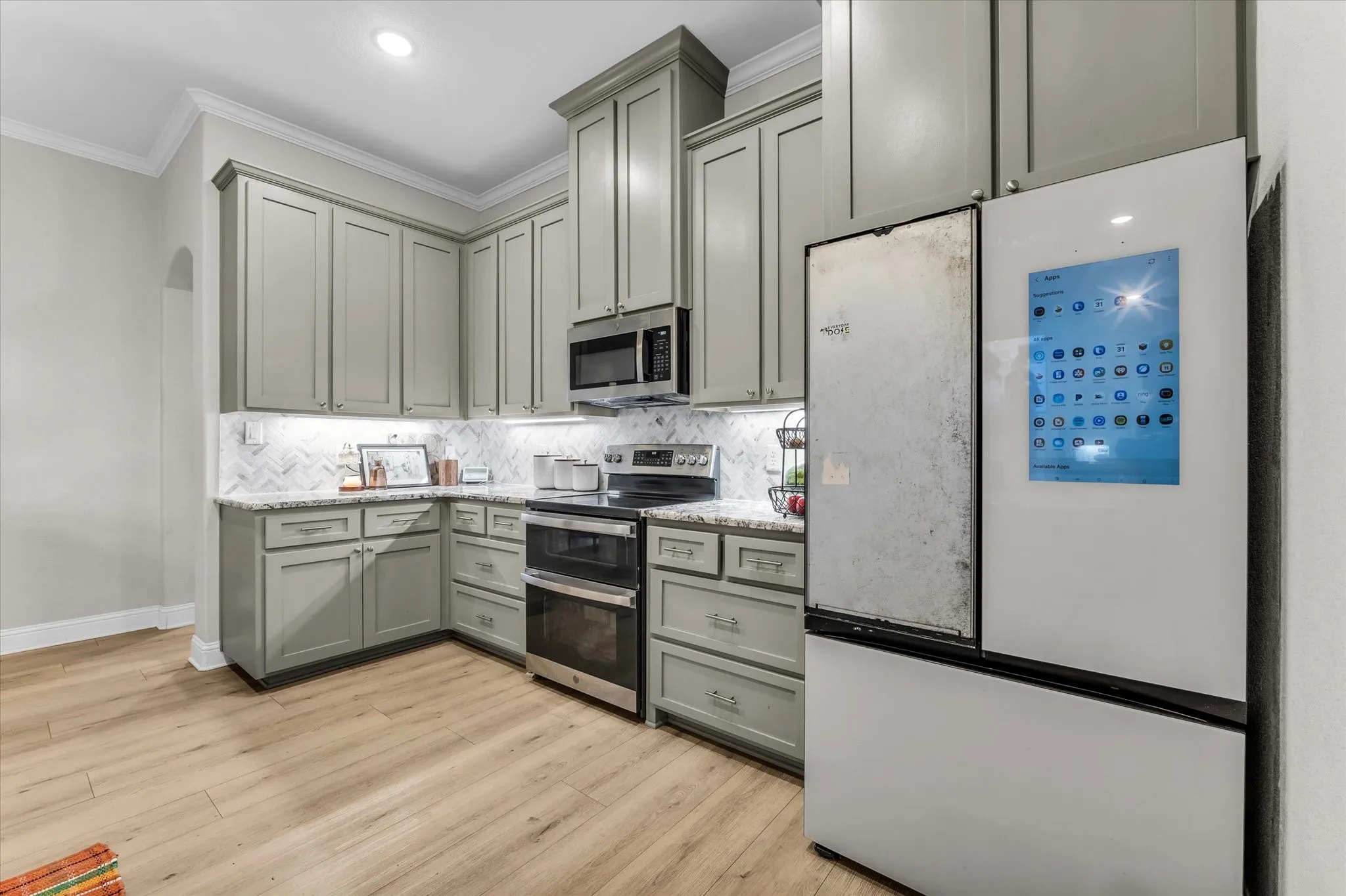 Kitchen featuring L-shaped cabinetry with under-cabinet lighting, stainless steel appliances, a tile backsplash, and wood-finish flooring