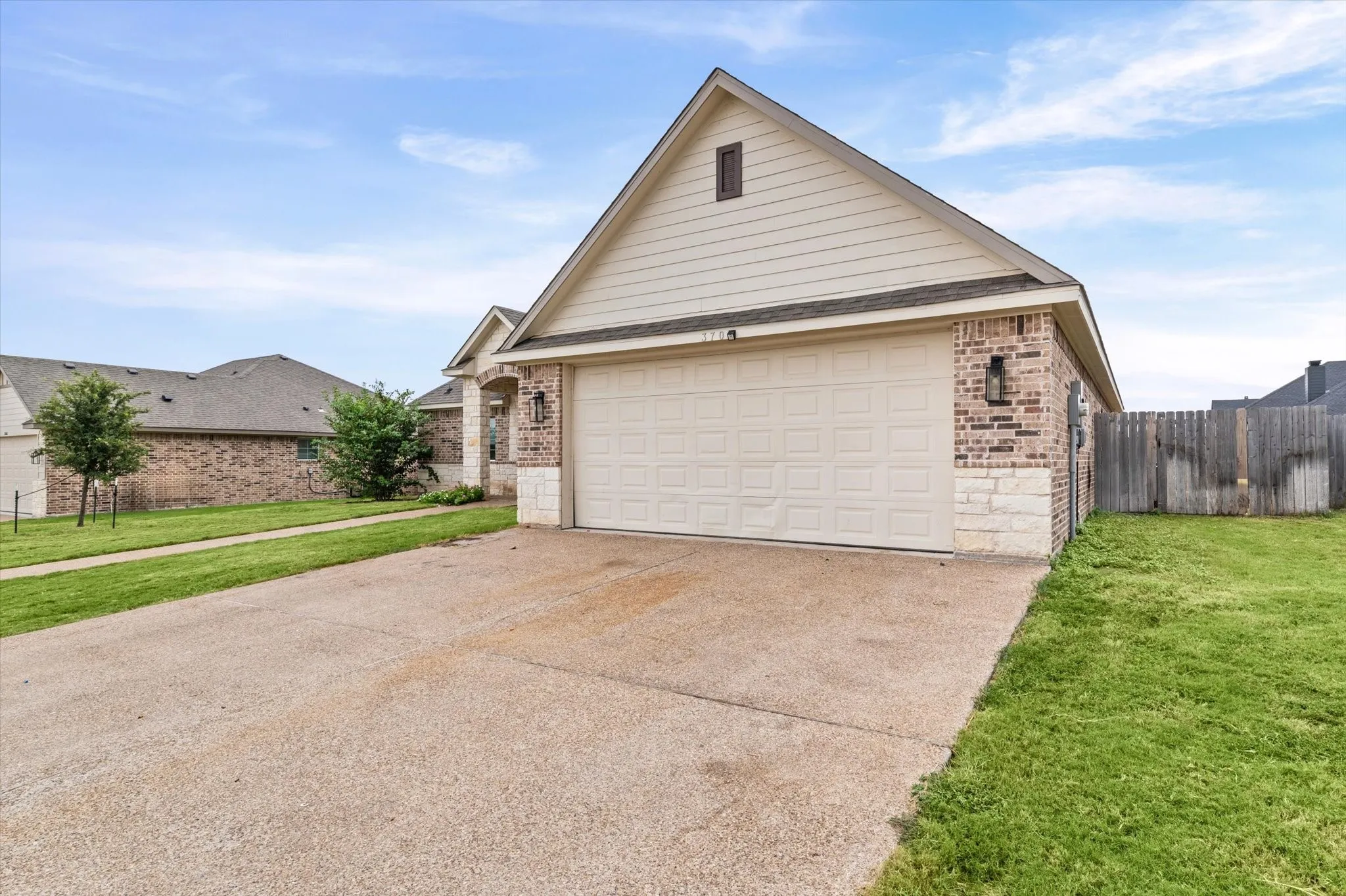 Exterior featuring a two-car garage, brick and stone facade, horizontal siding, and a gabled roof