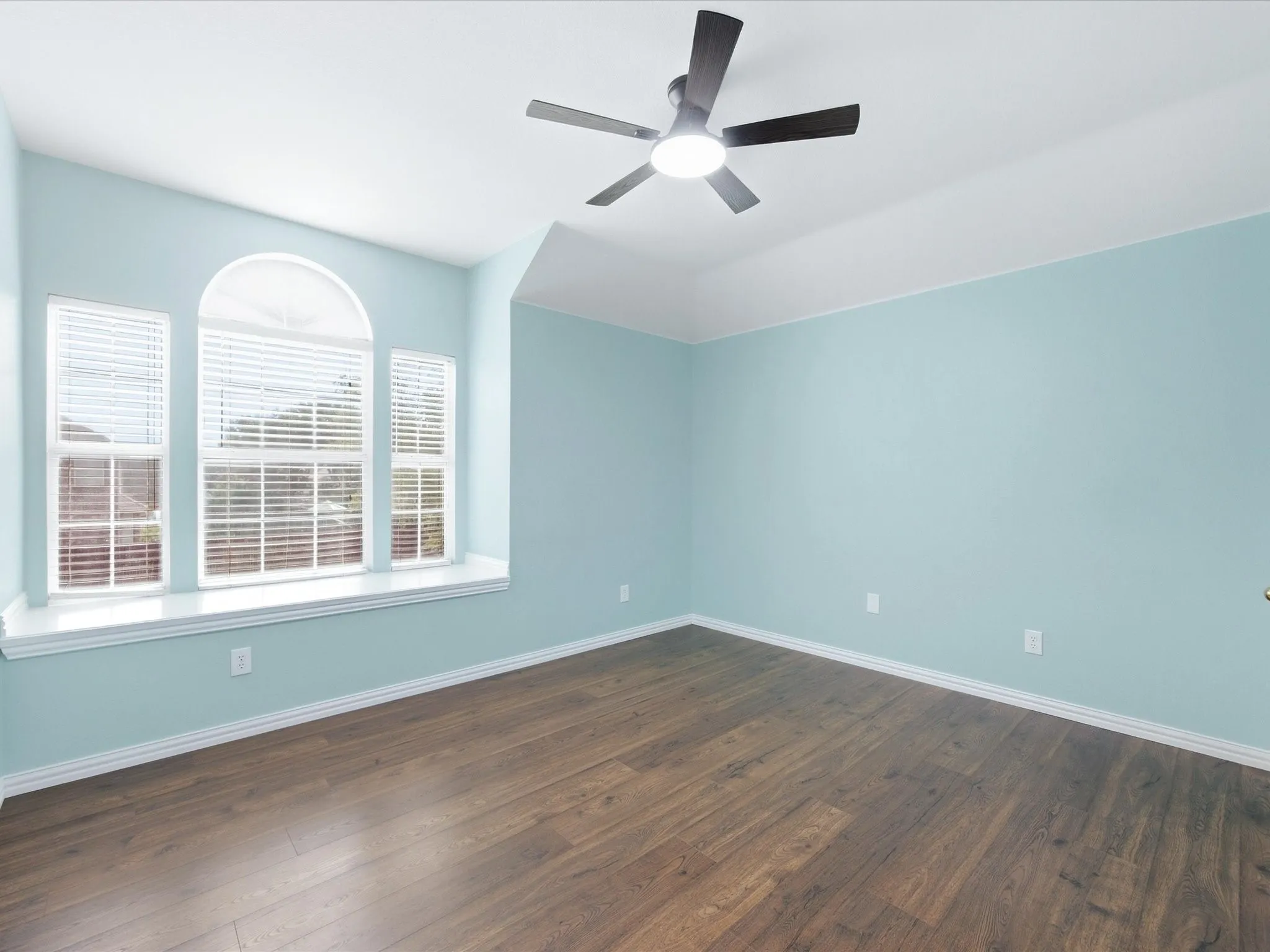Tray ceiling with a ceiling fan, wood-finish flooring, and a window seat with three windows, including an arched window