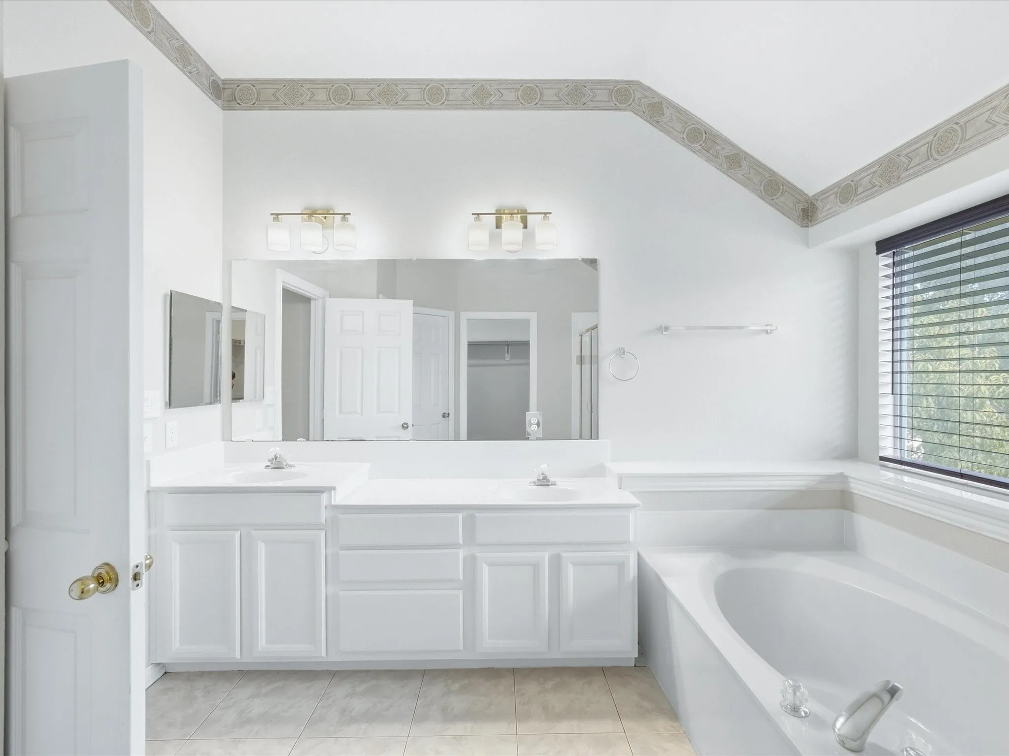Double vanity with white cabinetry and integrated sinks, large soaking tub, and tiled flooring