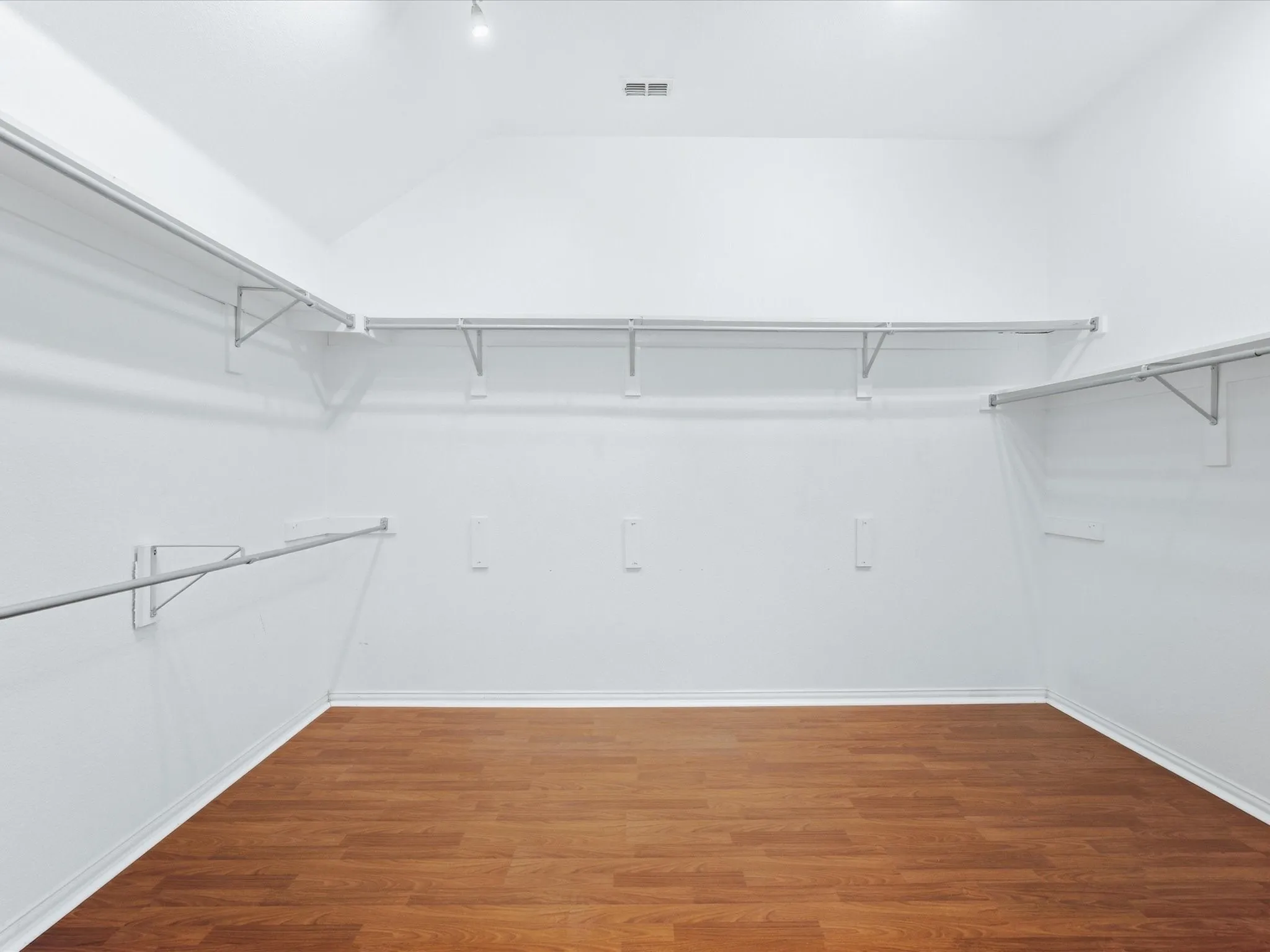 Spacious walk-in closet with vaulted ceiling, multiple hanging rods, integrated shelving, and wood-finish flooring