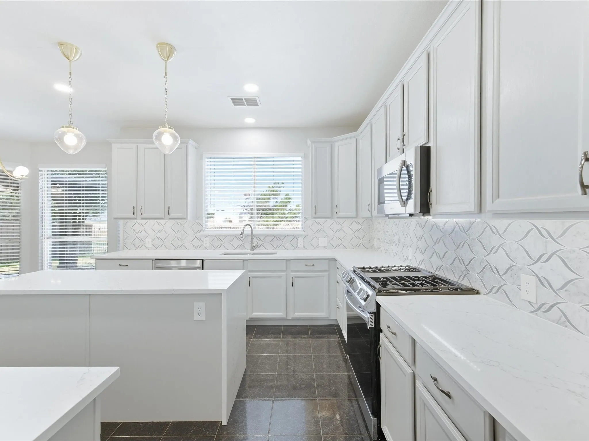 Kitchen featuring white cabinetry, white countertops, stainless steel appliances, a tiled backsplash, and dark tile flooring