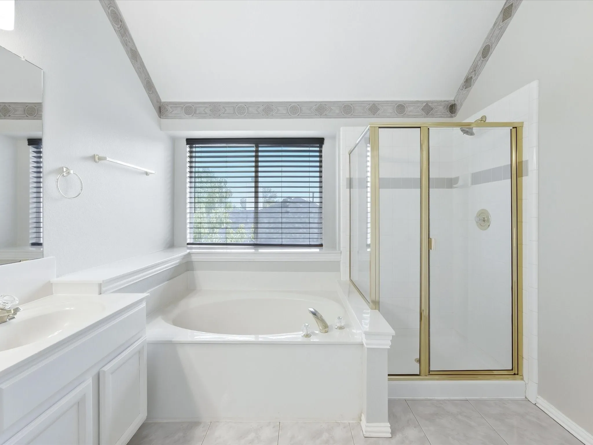 Built-in soaking tub, separate standing shower with gold-tone frame, single vanity with integrated sink, and horizontal window blinds