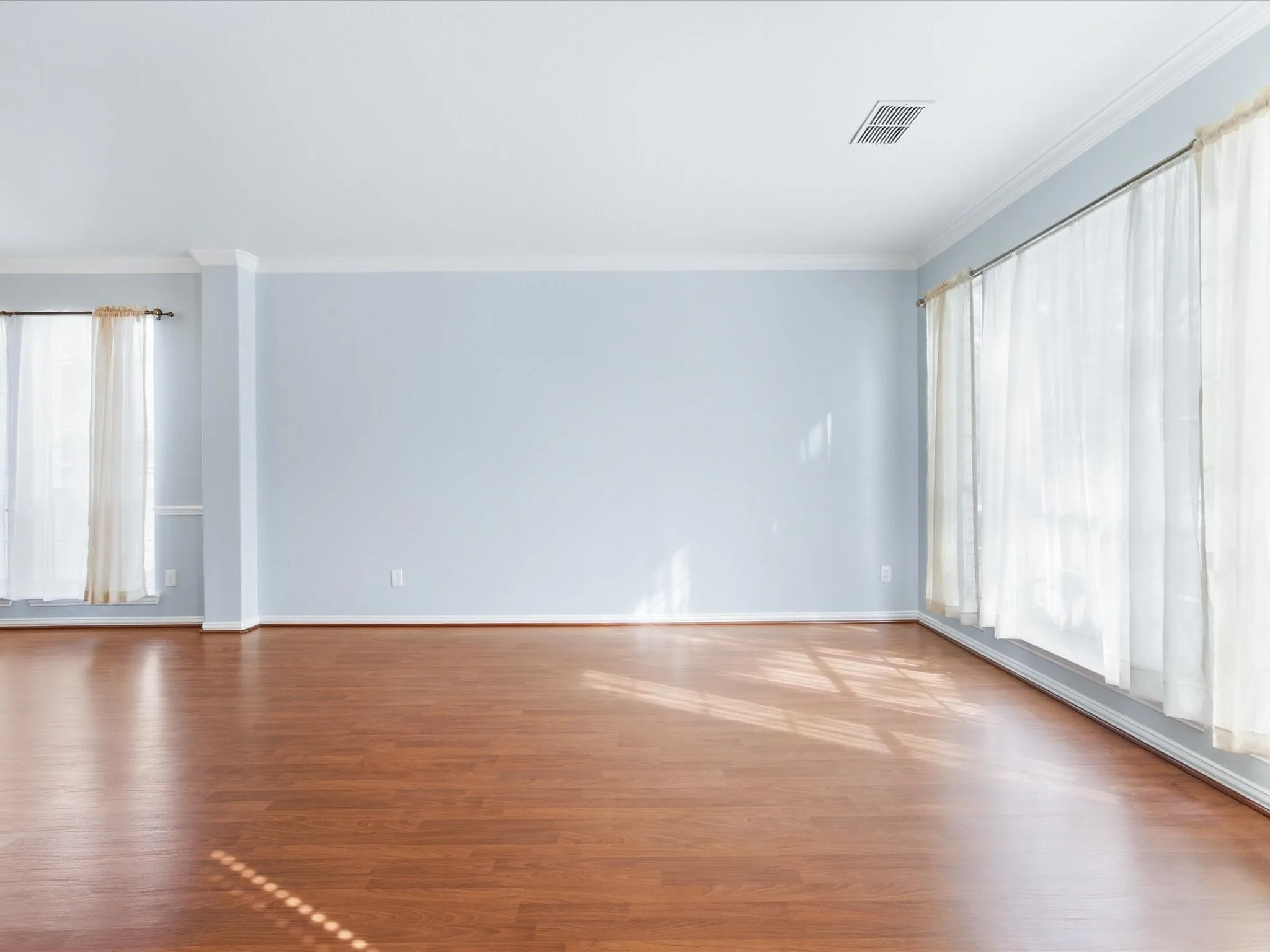 Wood-finish flooring, light blue wall paint, multiple large windows, white crown molding, and white trim