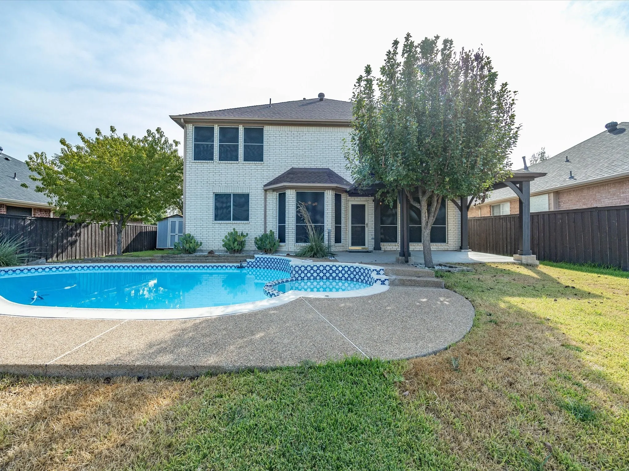Backyard featuring a built-in swimming pool with a concrete deck, pergola structure, privacy fencing, and a two-story brick exterior