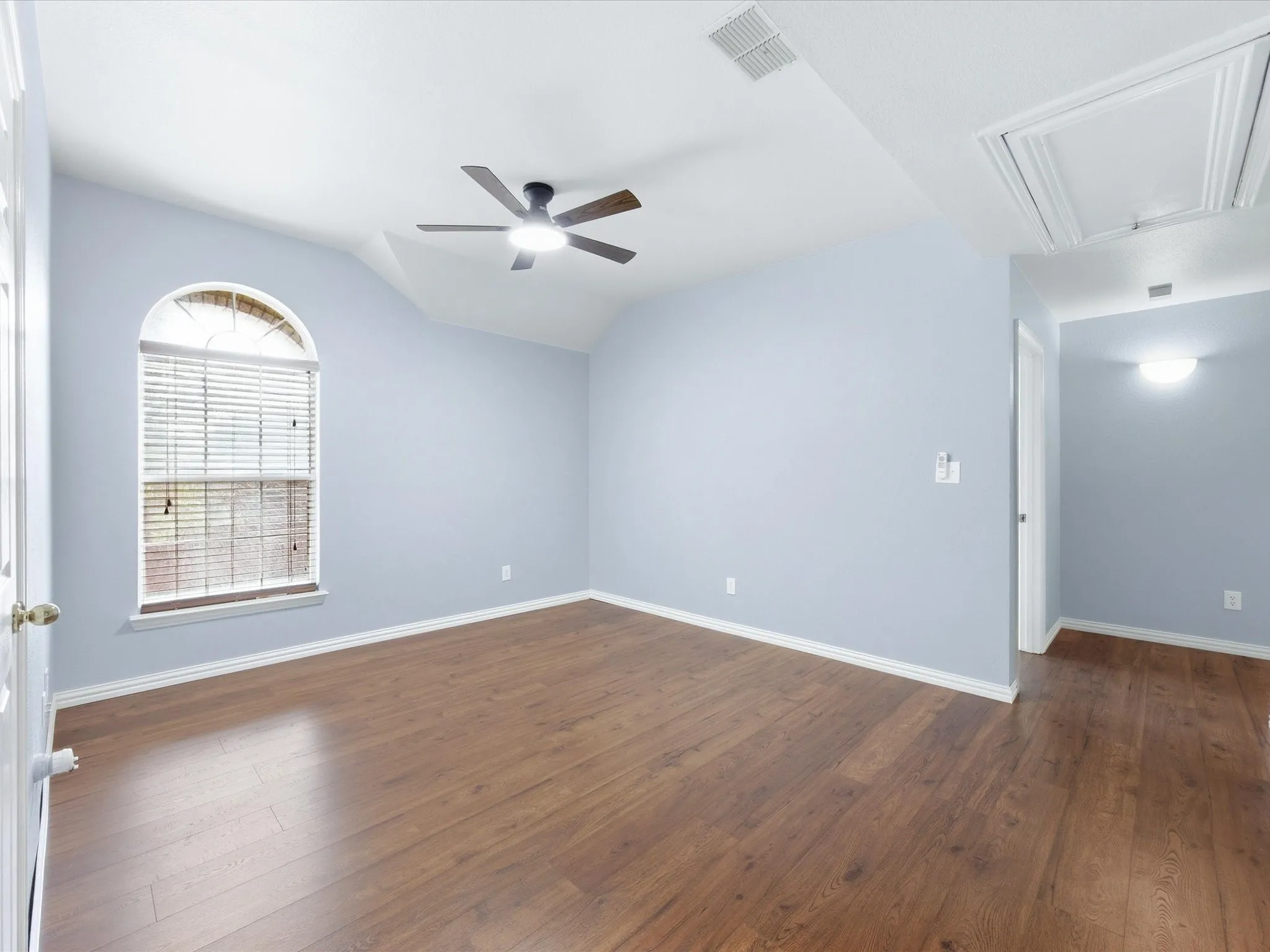 Wood-finish flooring throughout, arched window with blinds, ceiling fan, vaulted ceiling, and flush-mount lighting