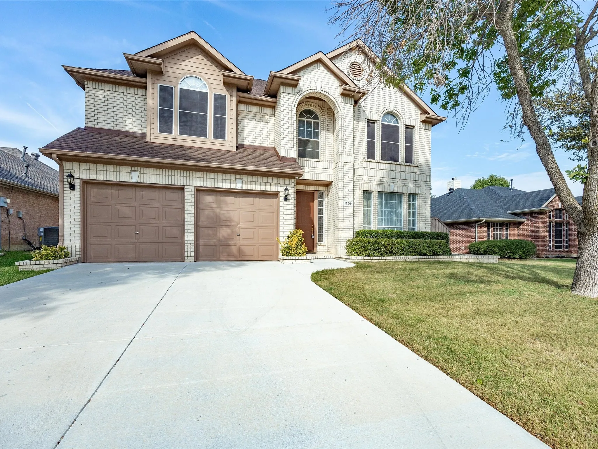 Light-colored brick exterior featuring a two-car garage, arched windows, and a concrete driveway