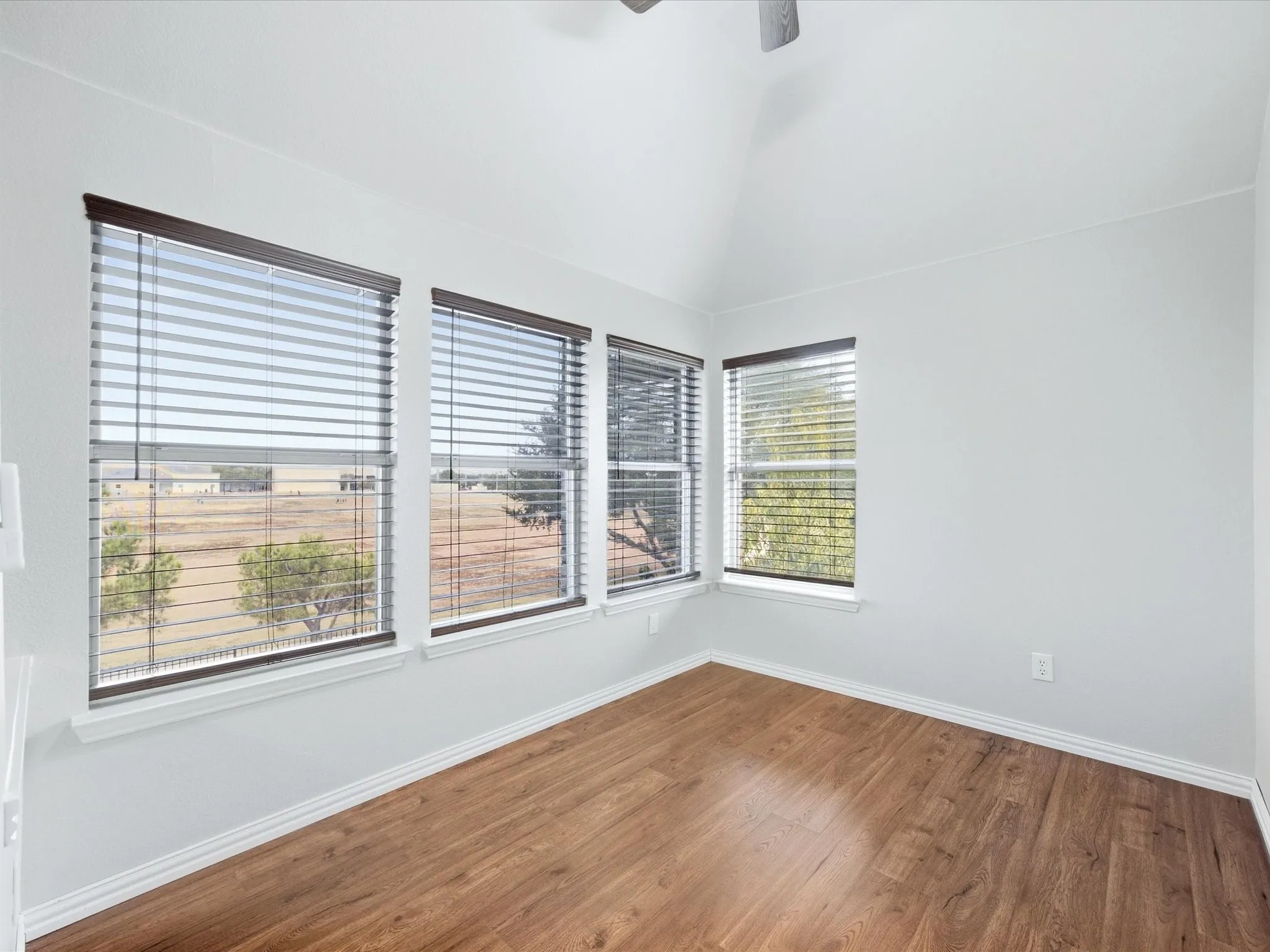 Vaulted ceiling with a ceiling fan, multiple windows with blinds, and wood-finish flooring